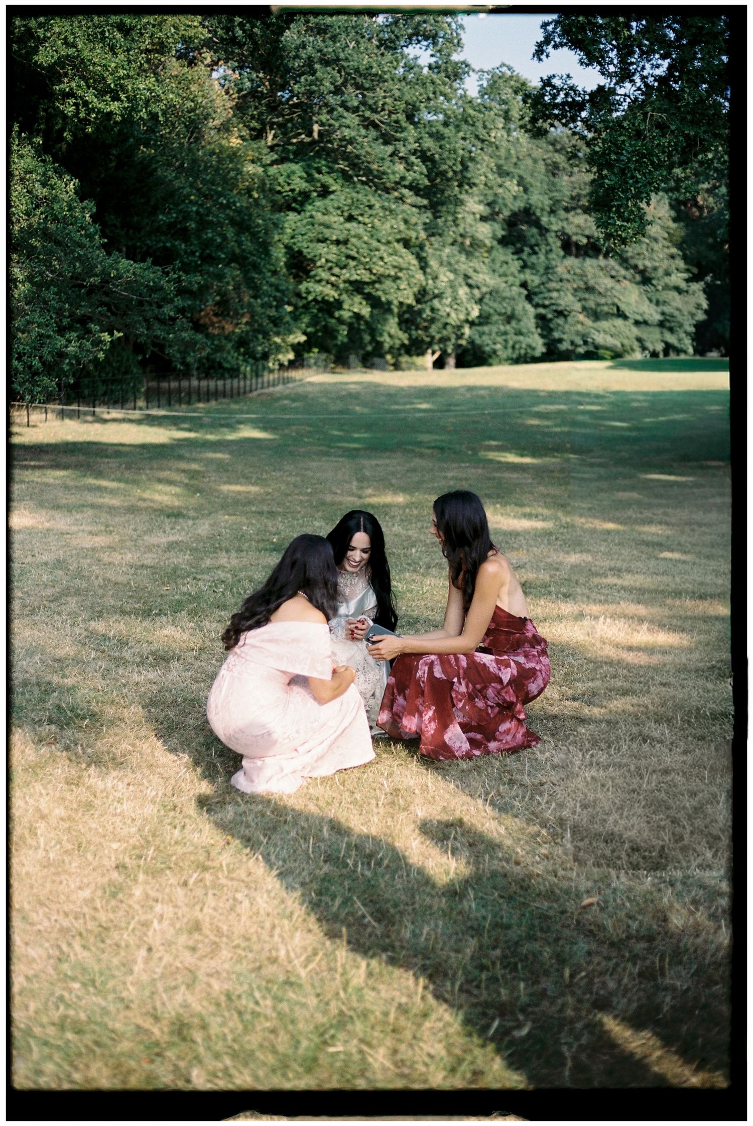 Three friends sitting on grass having a picnic in a sunny park.
