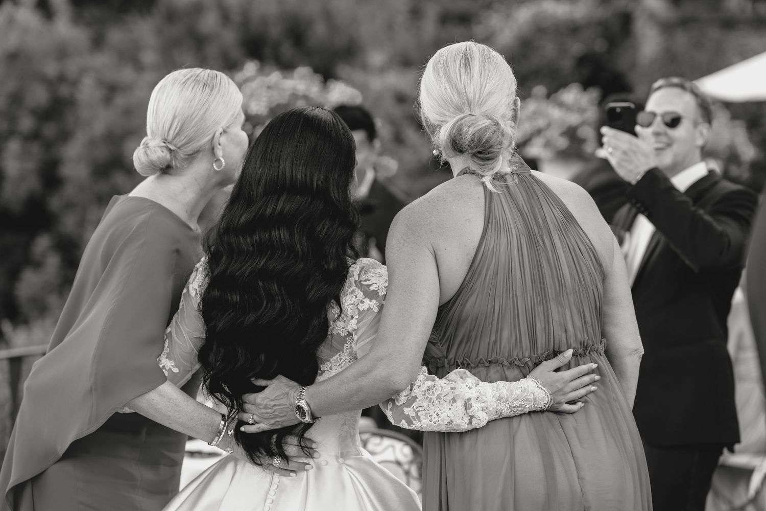 Wedding guests embracing during emotional reception moment in black and white.