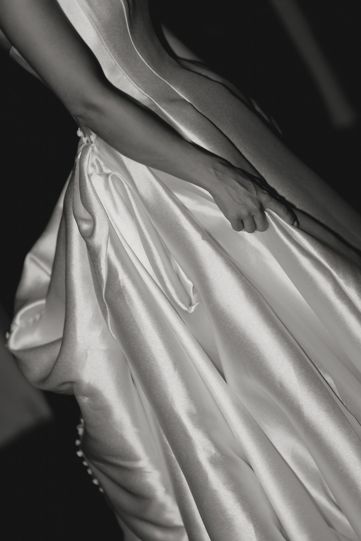 Black and white photo of a bride in a satin wedding gown, showcasing elegant fabric folds and pearl button details.