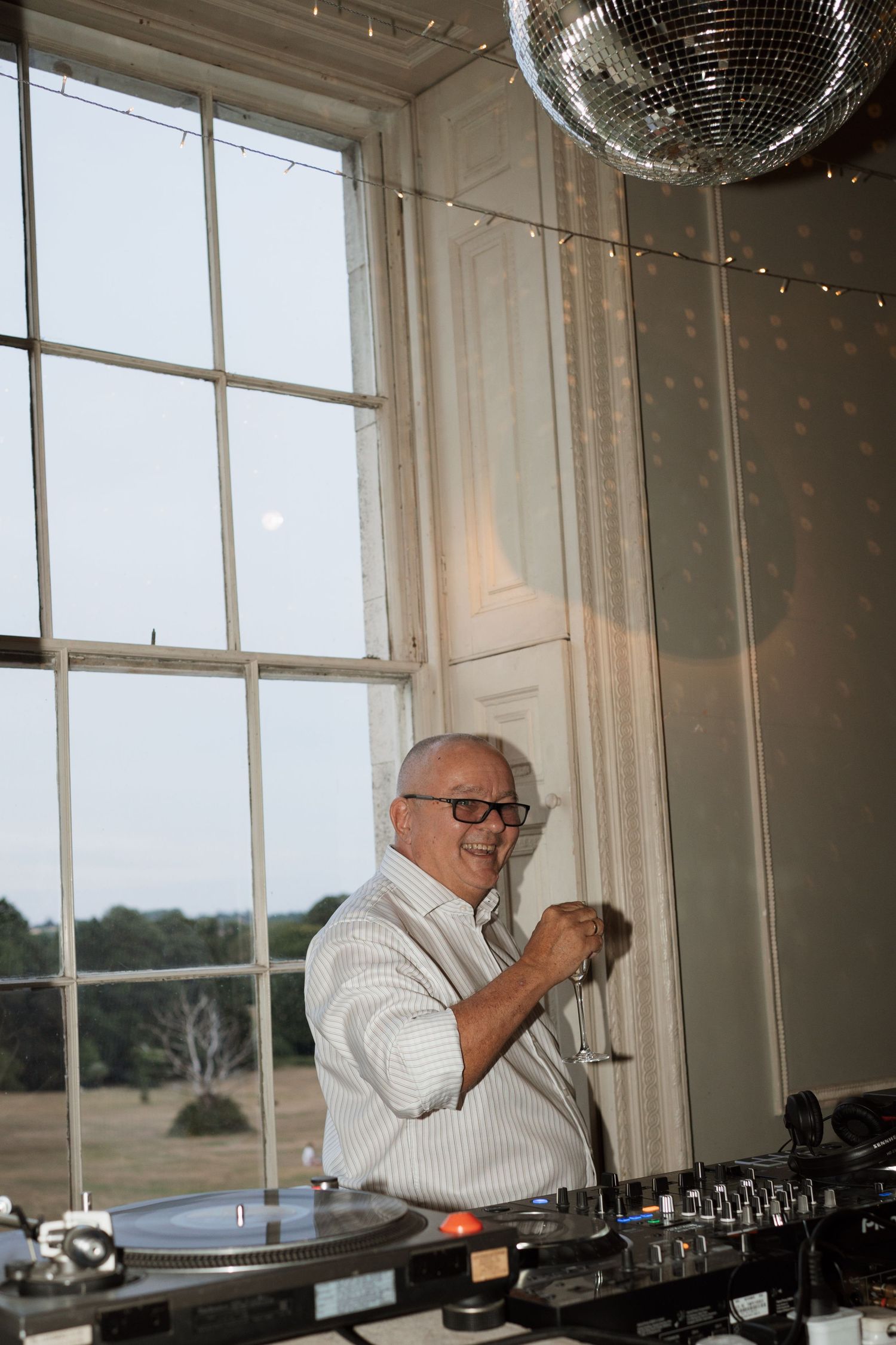 DJ working turntables at event with disco ball and window backdrop.