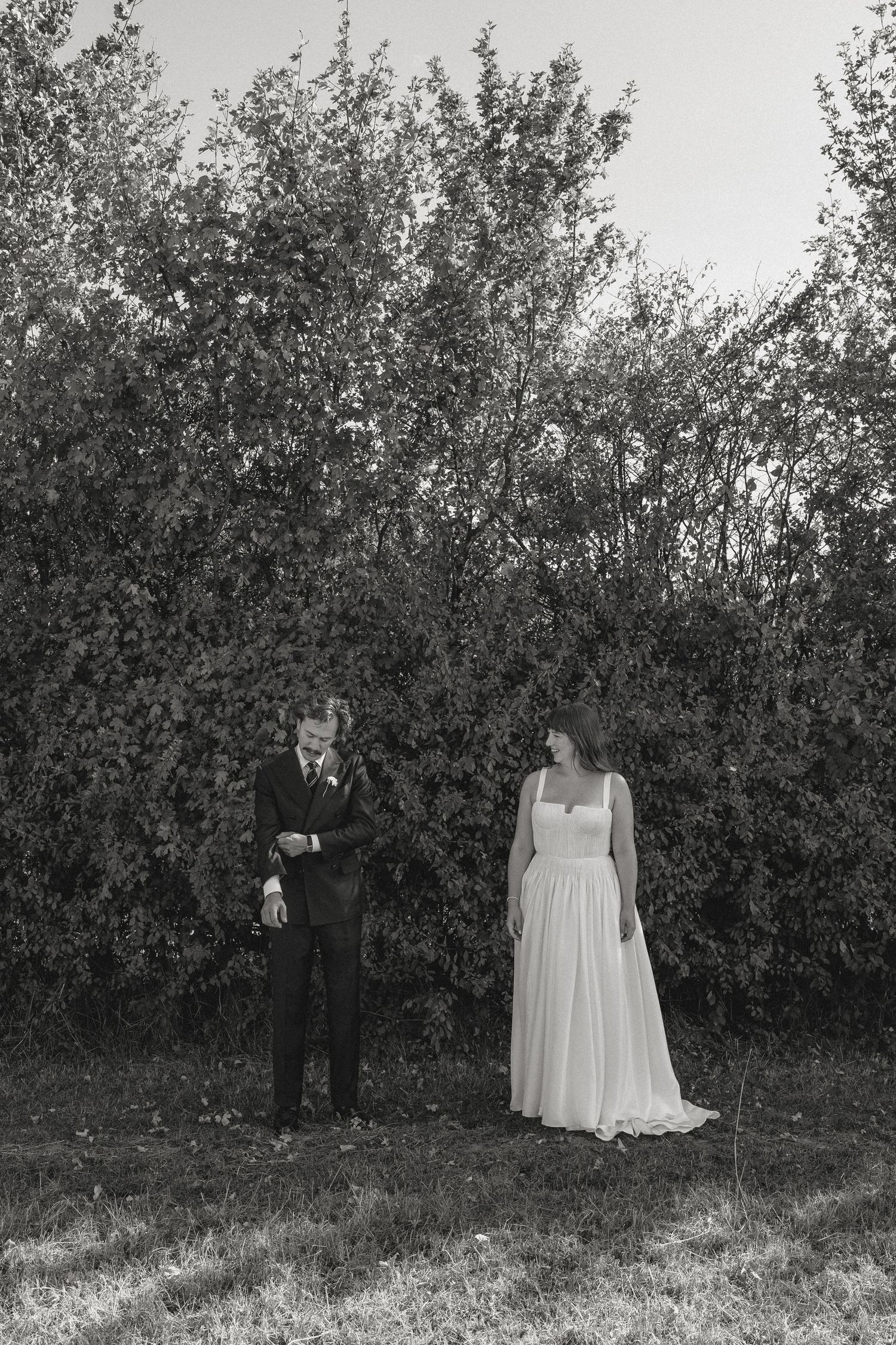 Black and white wedding portraits taken against a backdrop of lush bushes.