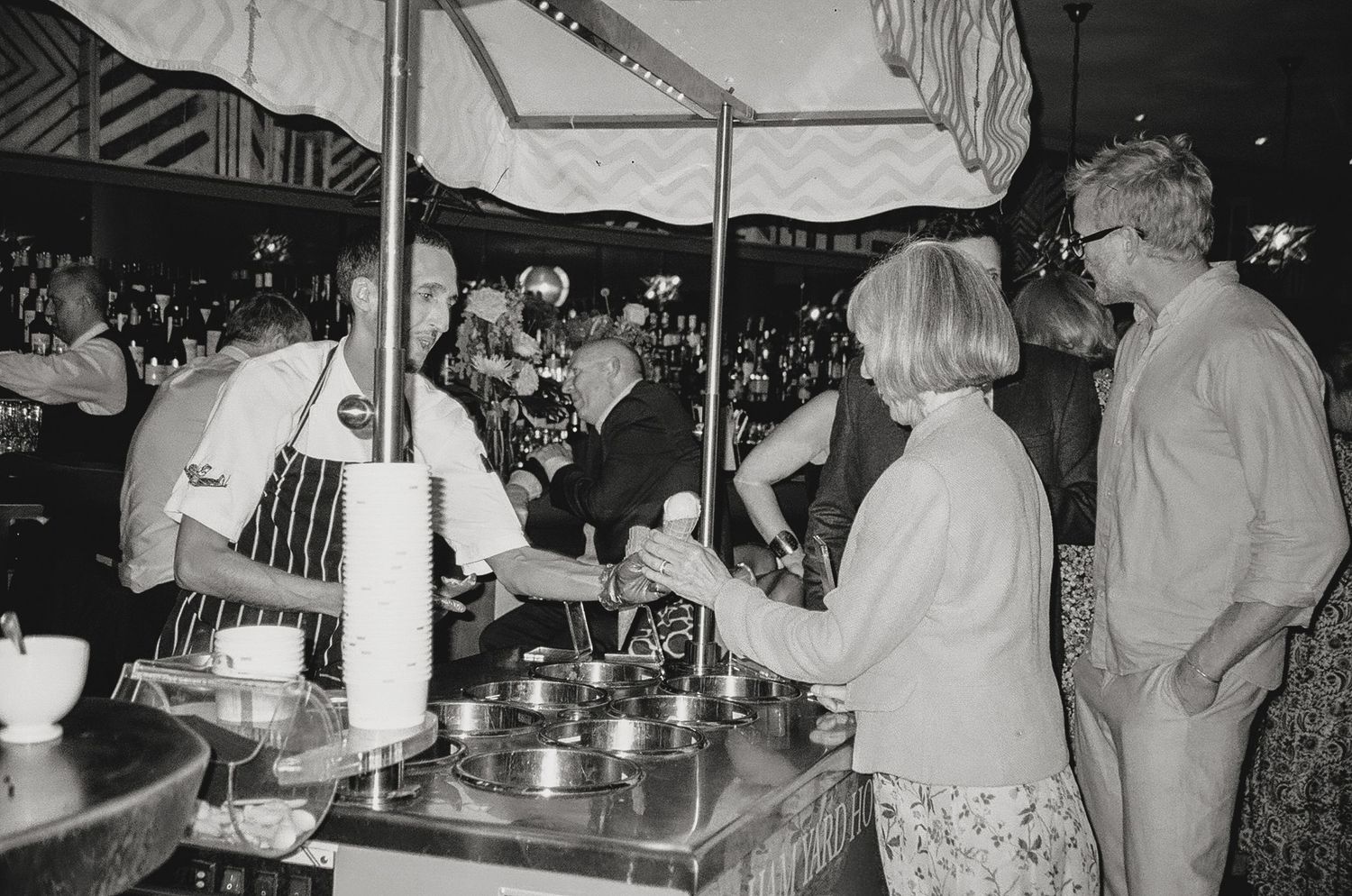 People gathered around a buffet station under a tent at an outdoor event.