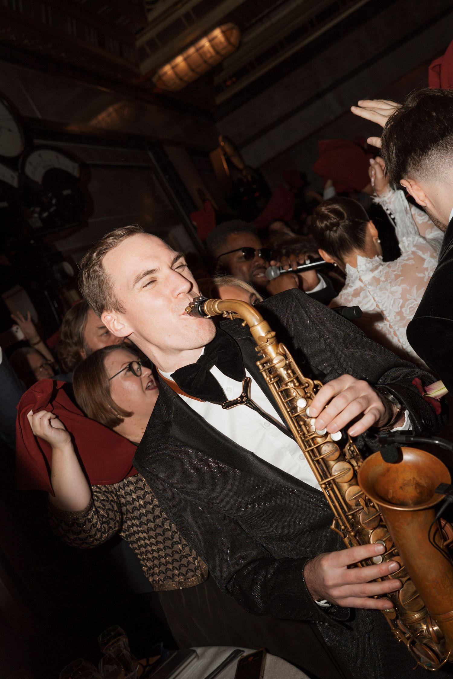 Musician in tuxedo plays saxophone during lively celebration.