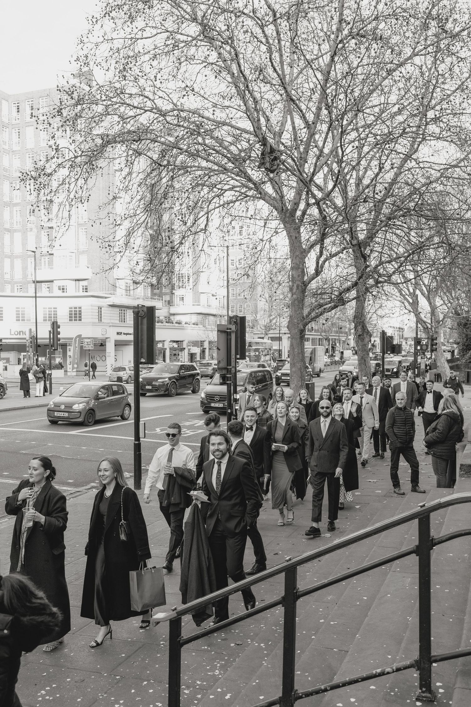 People walking along a tree-lined street in vintage black and white photography.