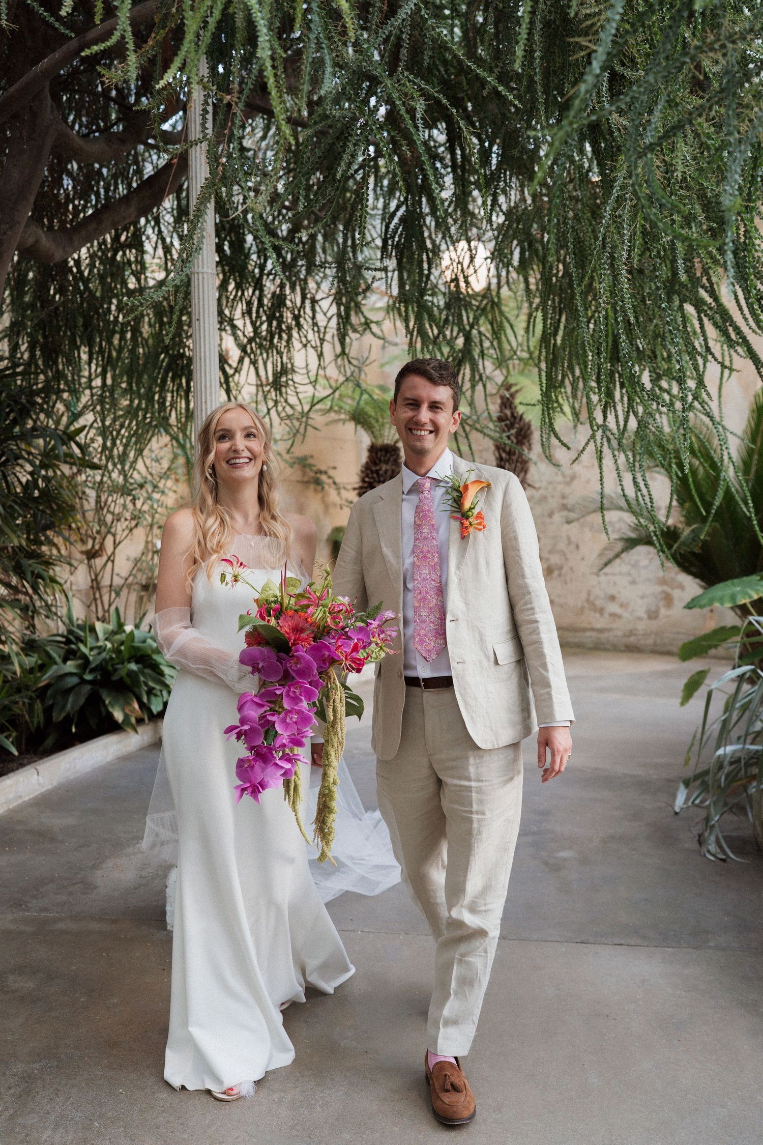 Wedding couple walking together in a covered walkway with tropical plants and stone walls.
