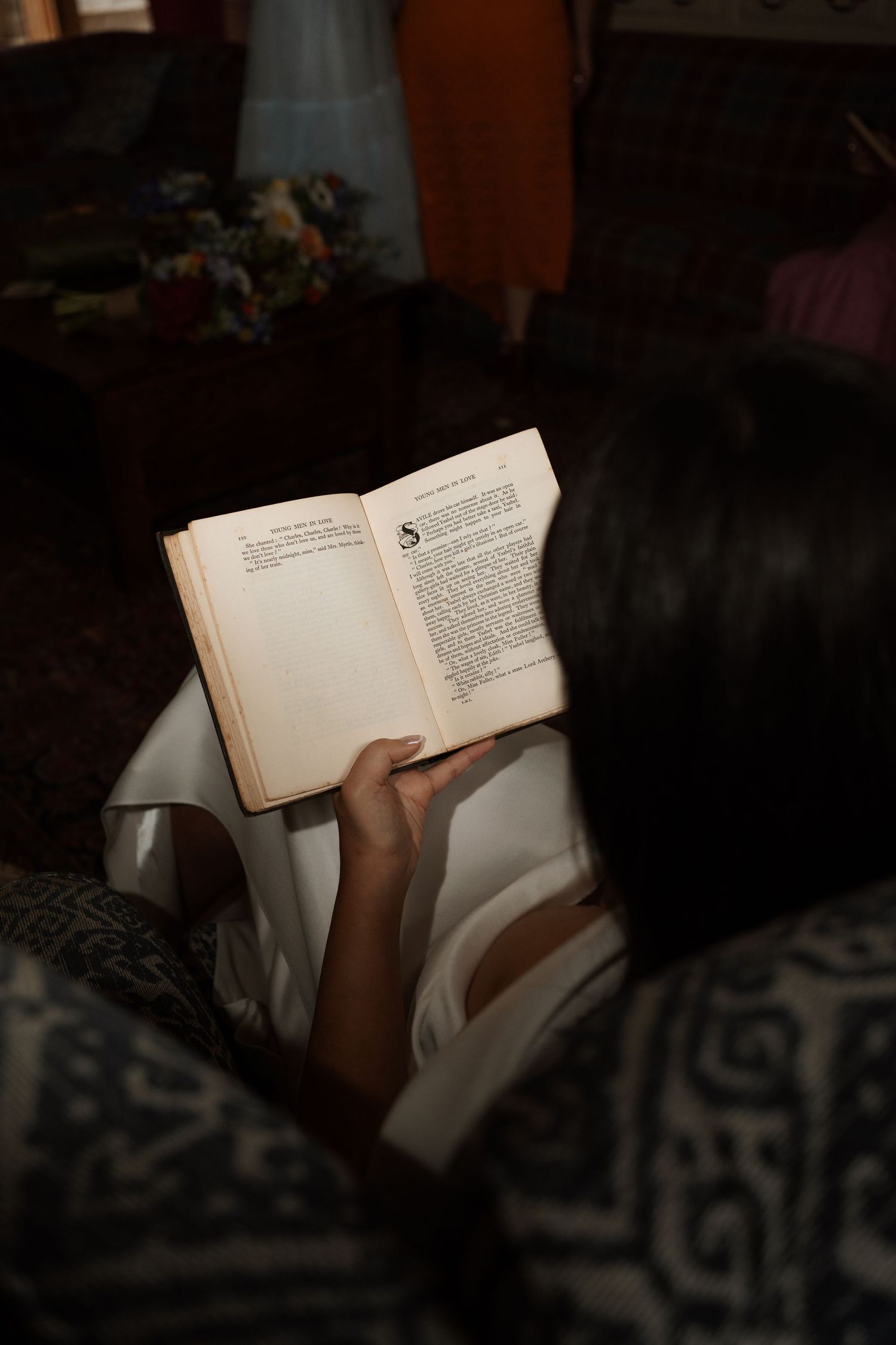 Hands holding an open book in dim lighting, creating an intimate reading moment.