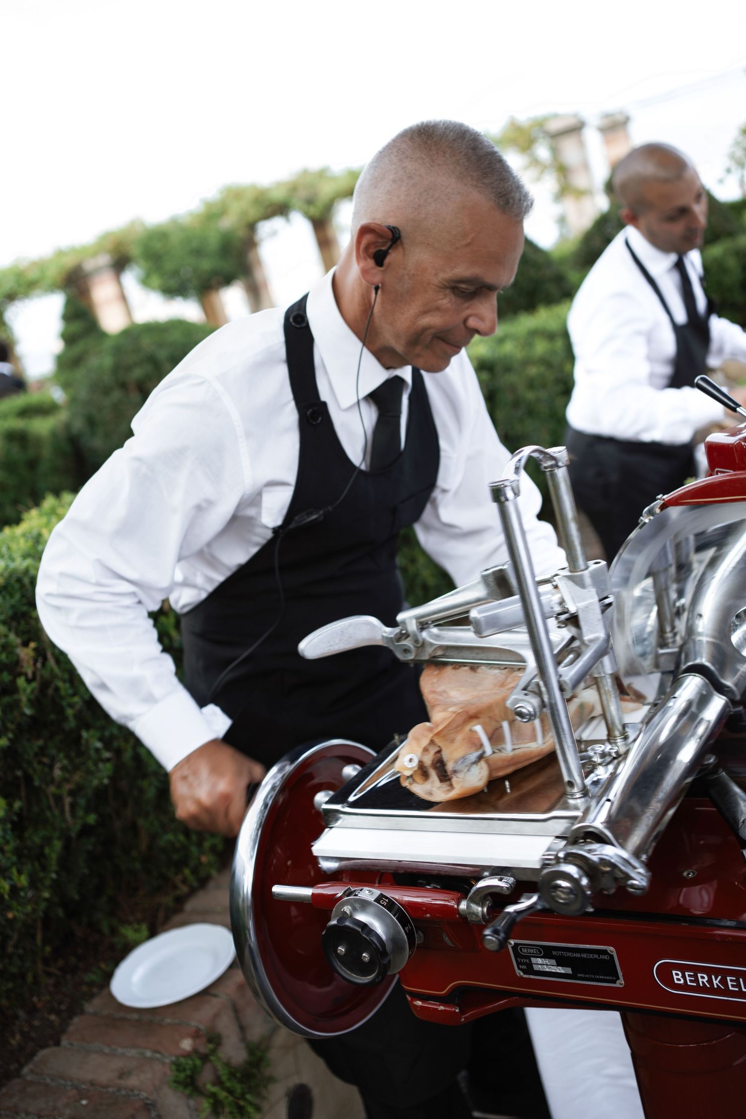 Server in formal attire operating an espresso machine at an outdoor event.