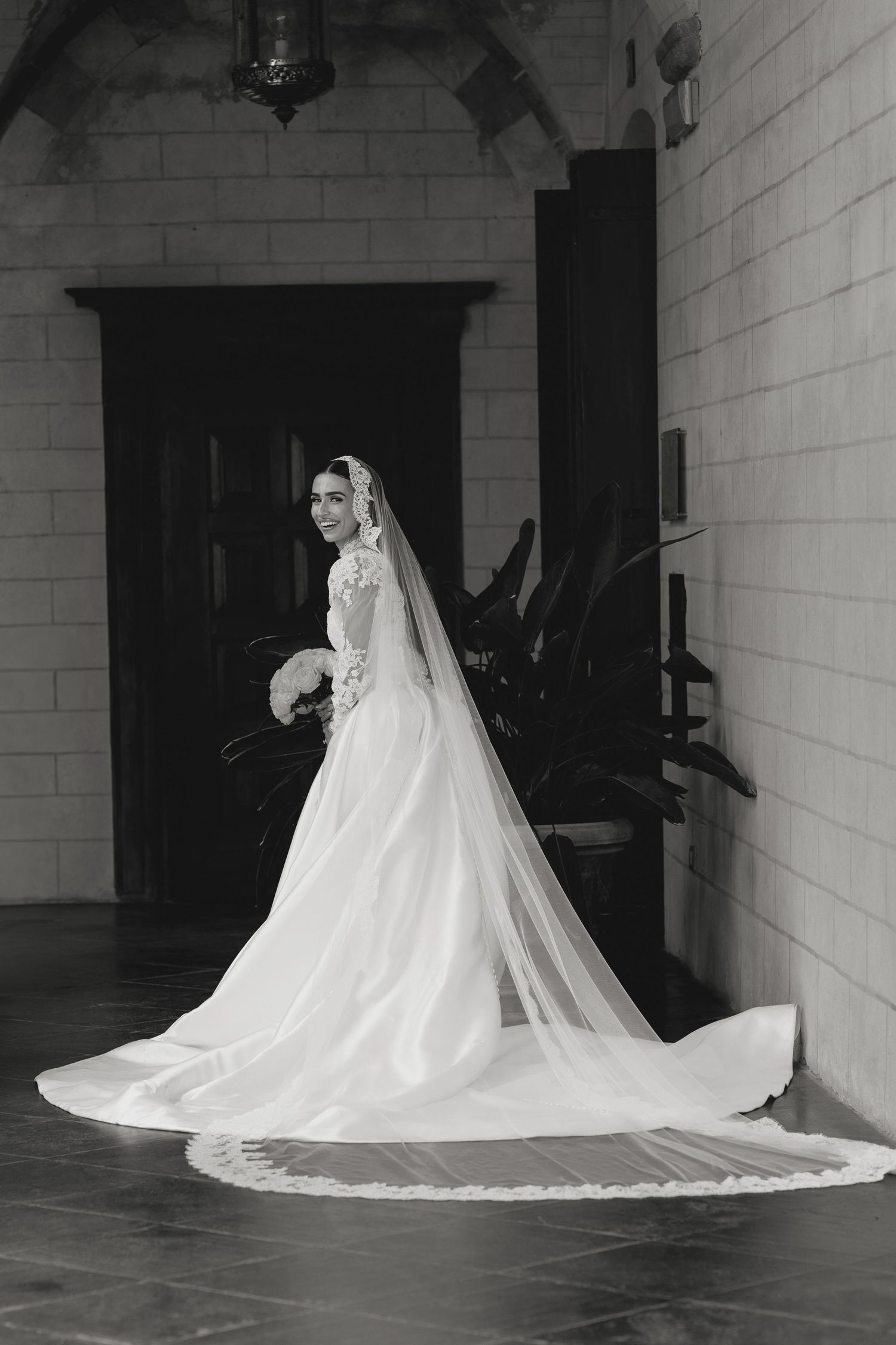 Dramatic black and white photo of a flowing wedding dress train against white walls.