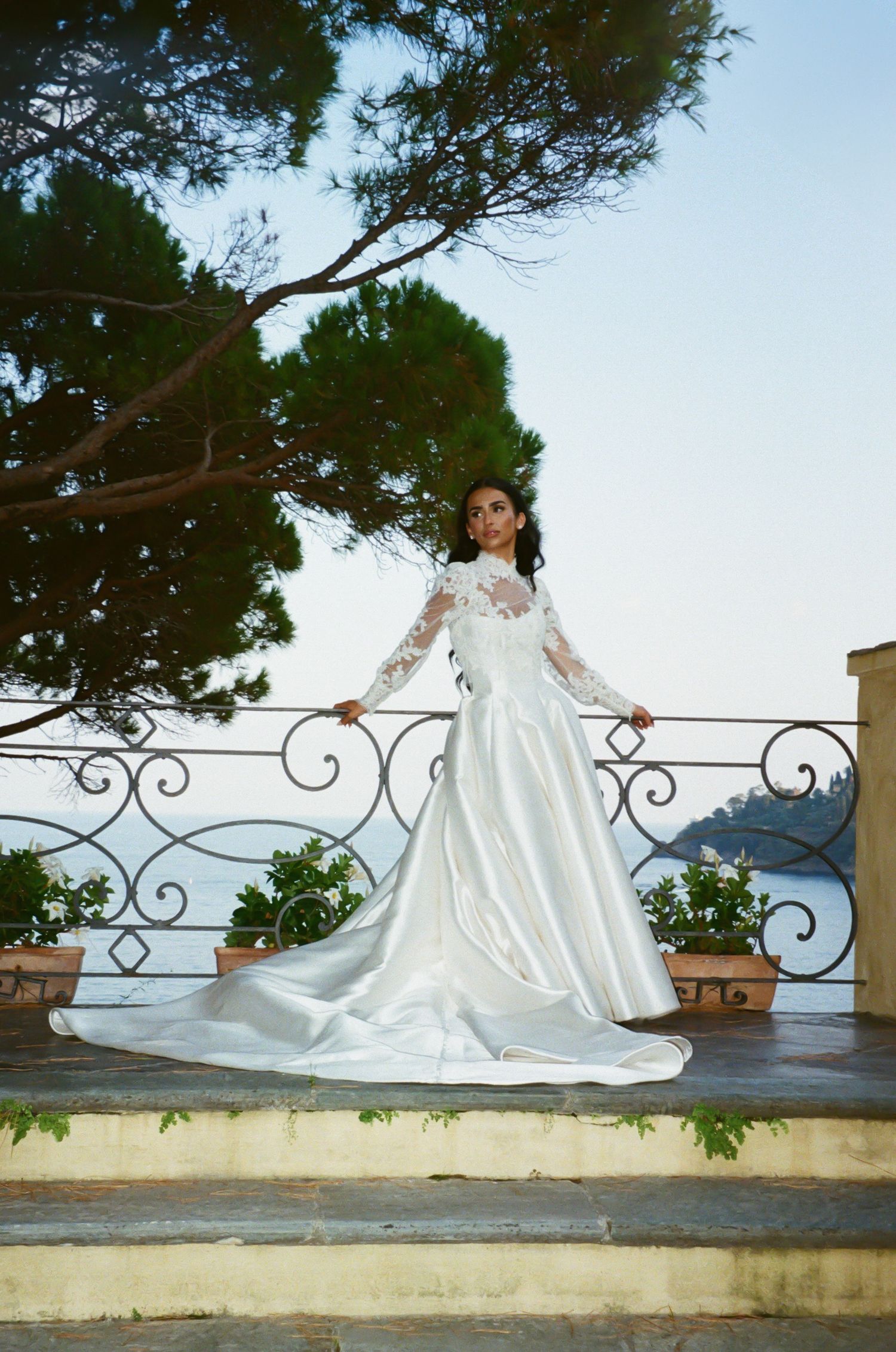 A bride in a flowing white gown poses elegantly along a Mediterranean balustrade.