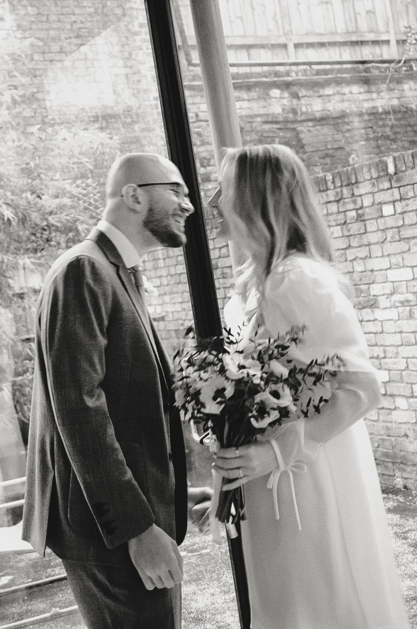 Couple sharing intimate moments against a brick wall backdrop with wedding bouquet.