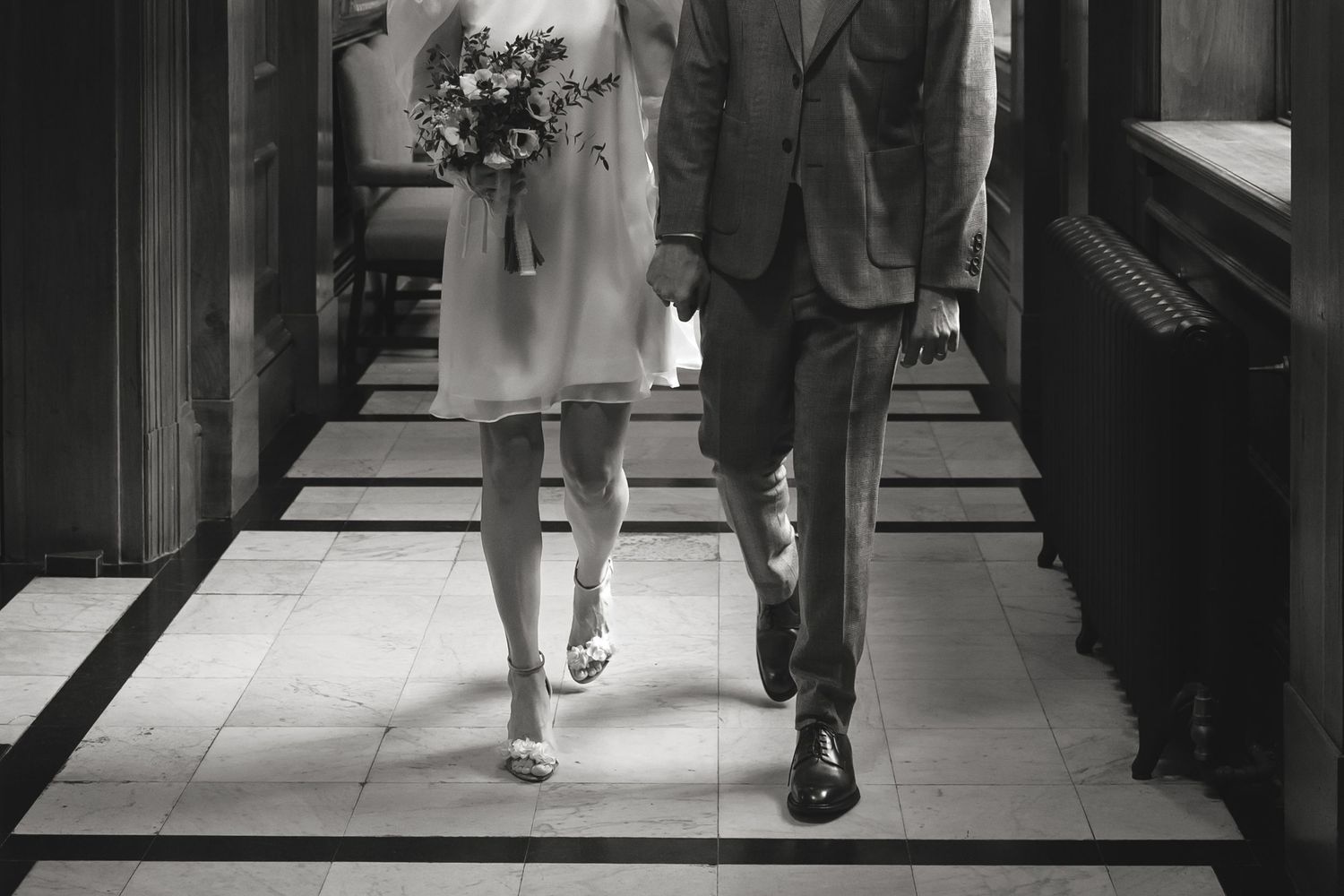 Black and white photo of couple walking through grand interior corridor.