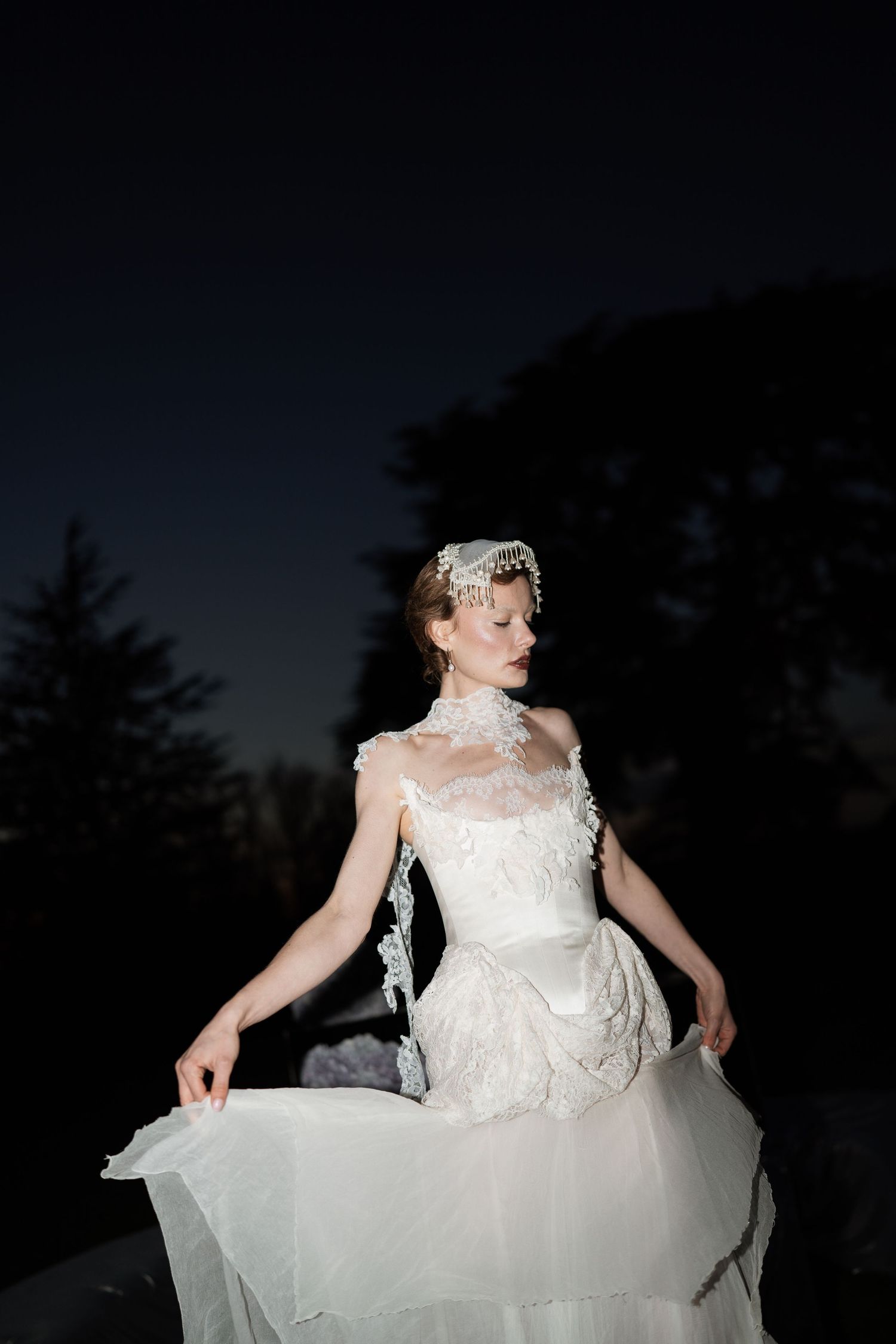 Dramatic nighttime portrait of bride in classic white gown against dark sky.