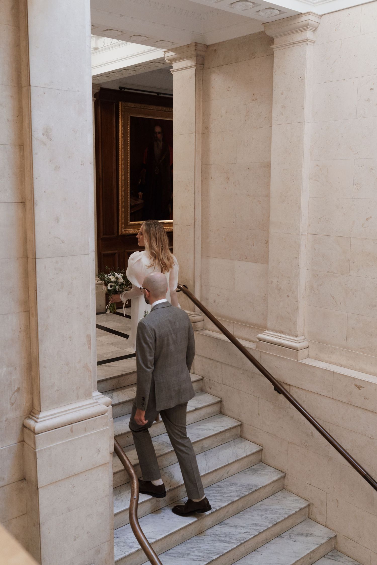 A couple ascending white marble stairs in a classic building interior.