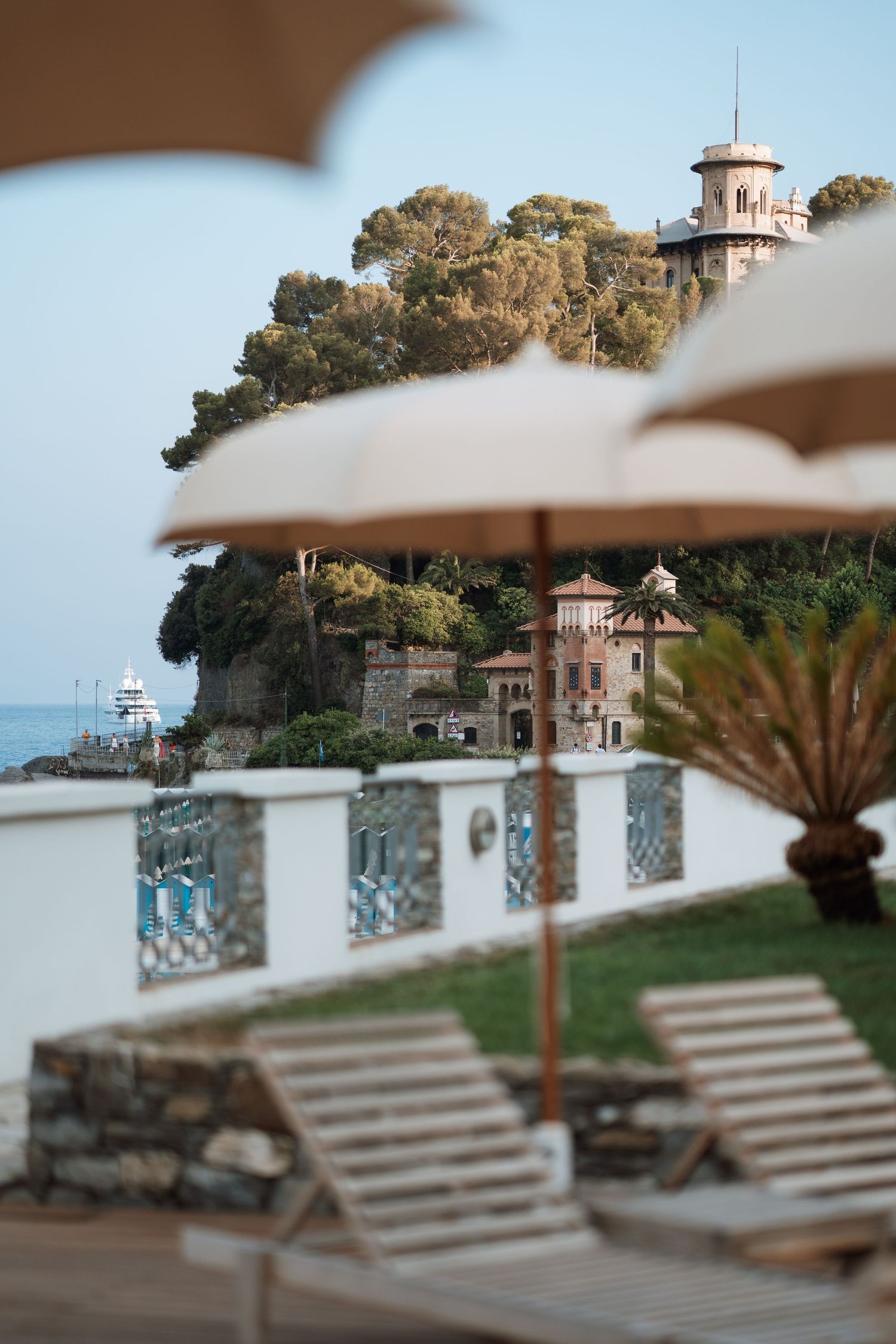 Luxurious beach lounge chairs overlooking a Mediterranean villa and coastline.