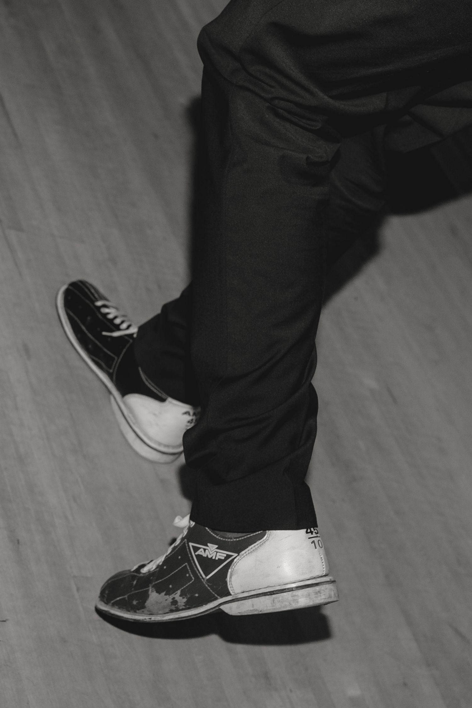Close-up shot of black pants and sneakers on a light wooden floor.