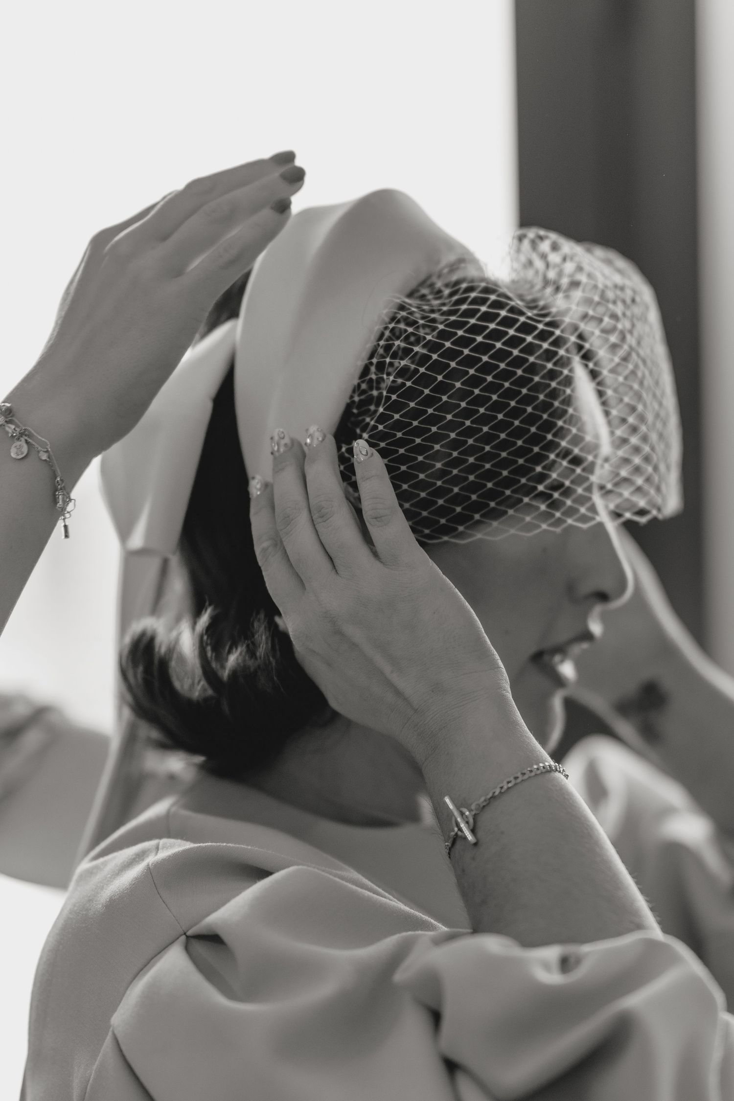 A vintage-inspired bridal look features a netted veil being adjusted in black and white photography.