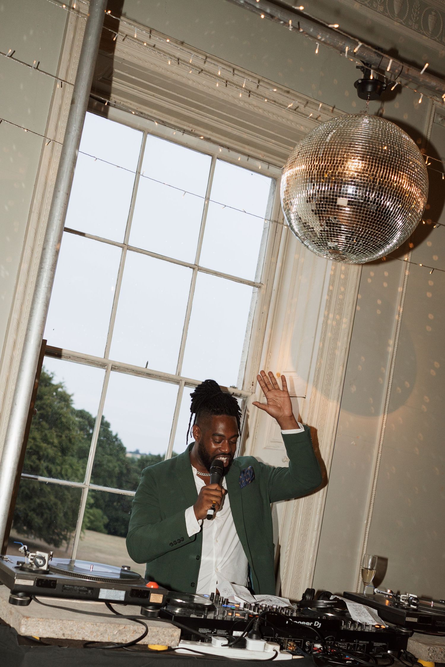 DJ performs under a disco ball at an elegant indoor venue with large windows.