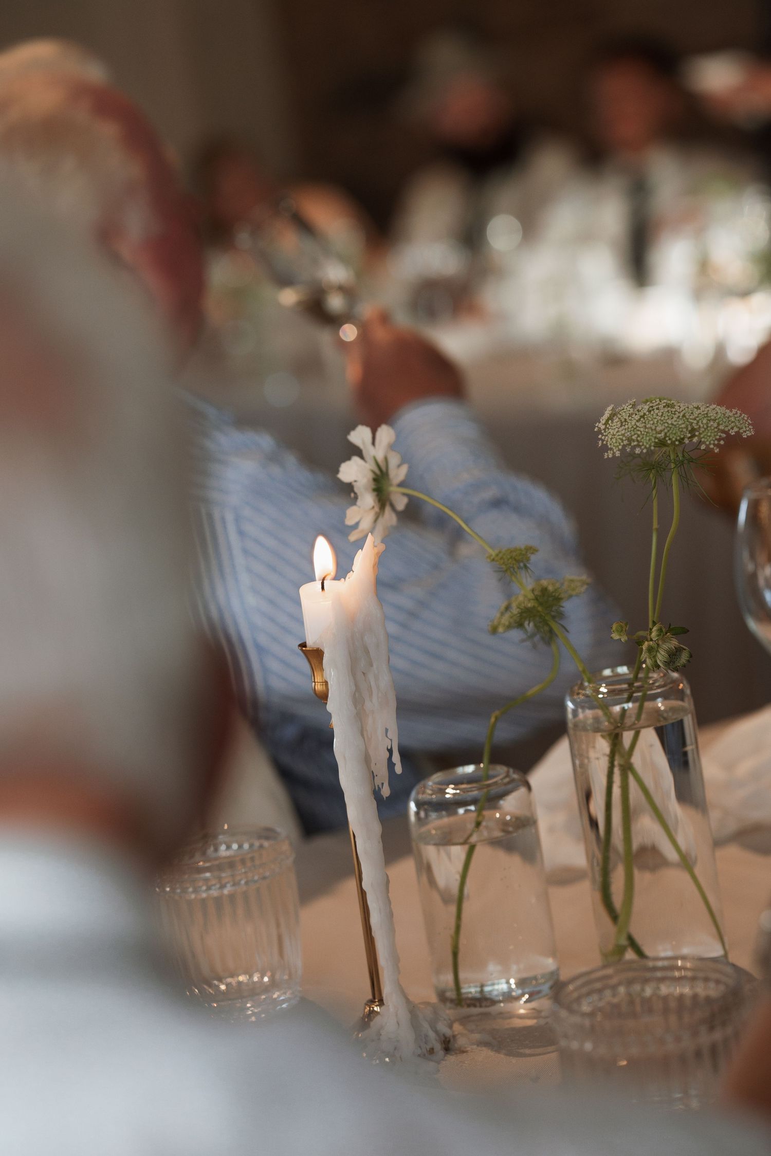 Elegant table setting with white candles and delicate floral arrangements at wedding reception.