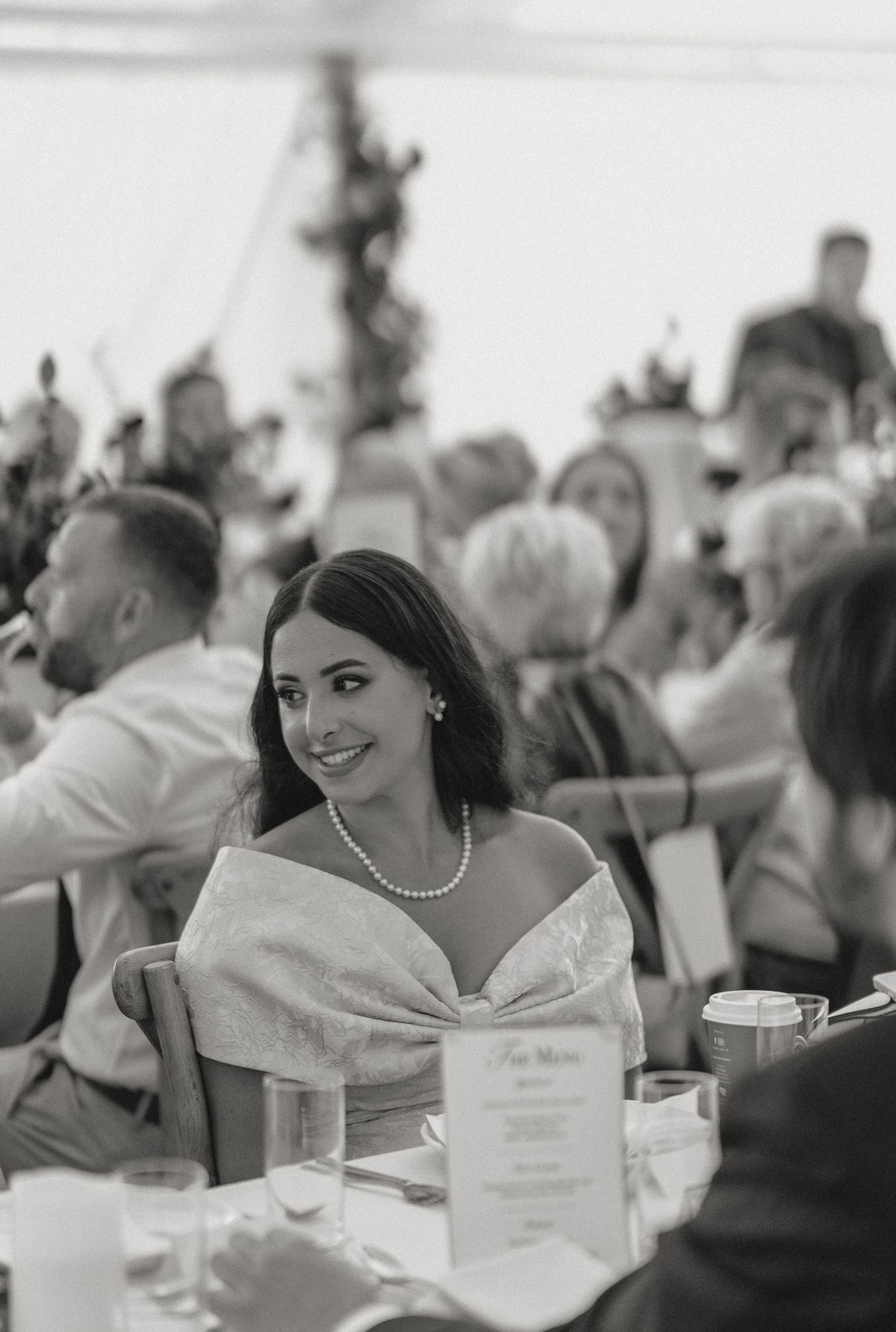 Black and white photo of wedding guests seated at reception tables with elegant place settings.