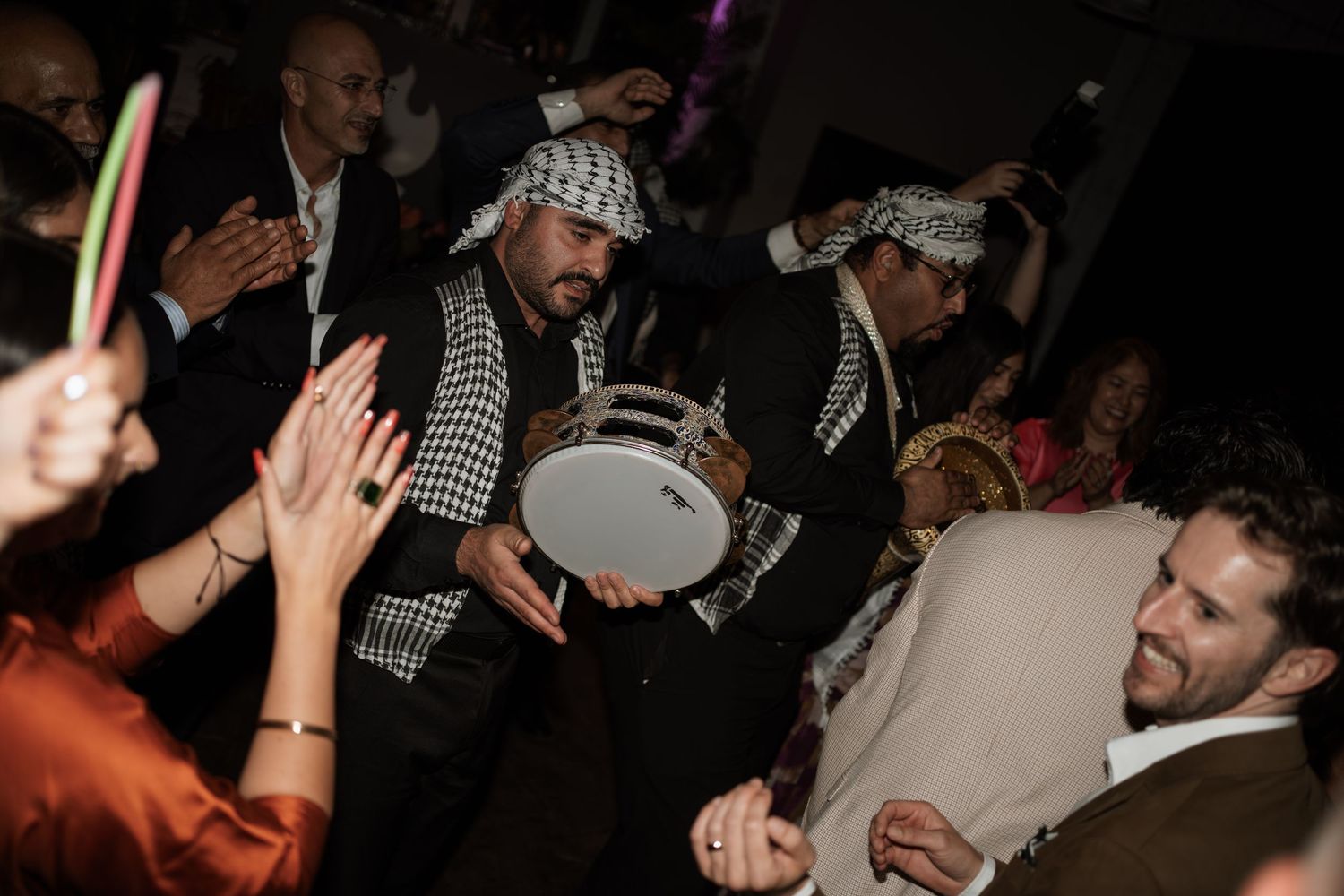 Lively party scene with drummers wearing traditional Middle Eastern scarves entertaining the crowd.