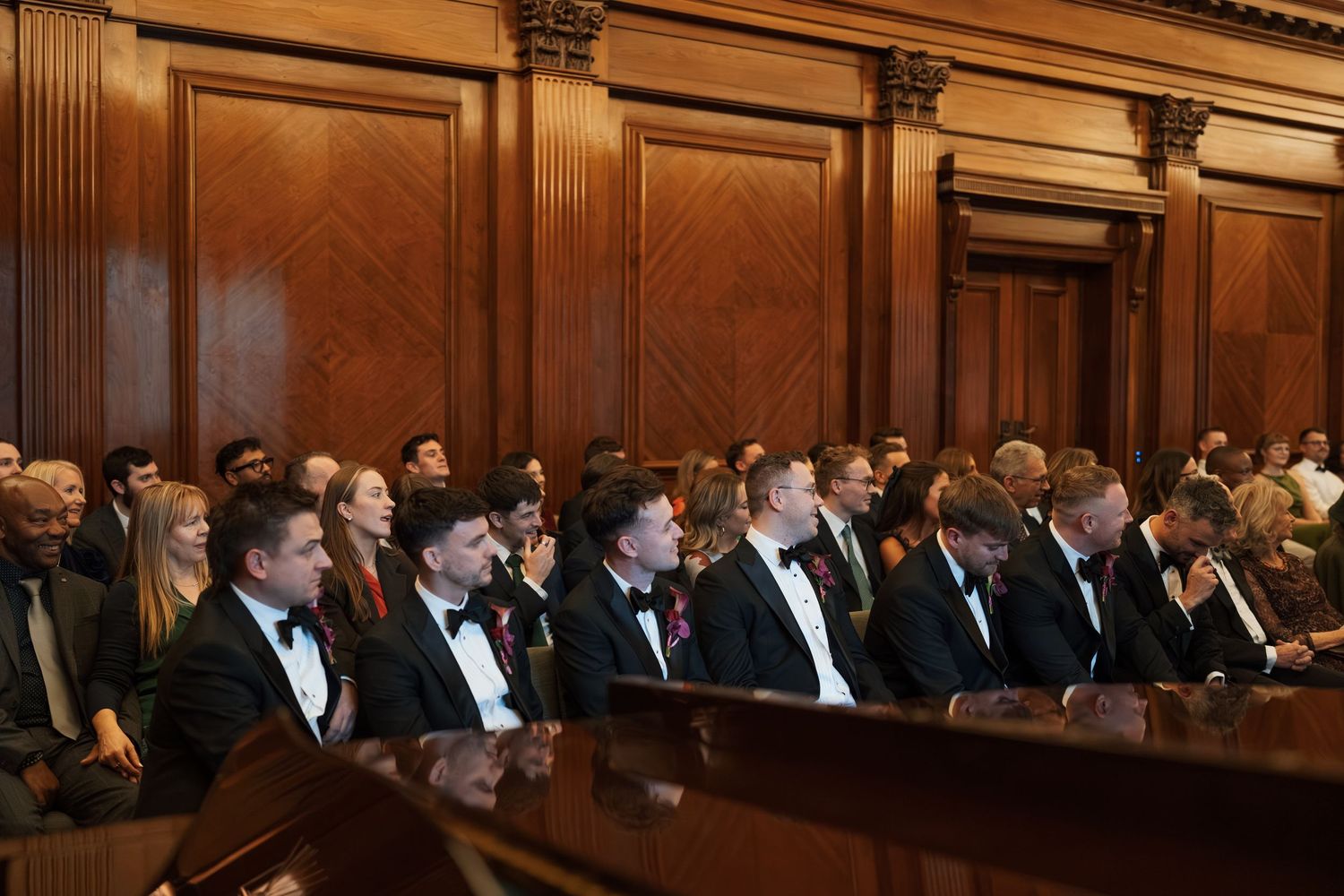 Formal gathering in a wood-paneled hall with attendees seated in rows.
