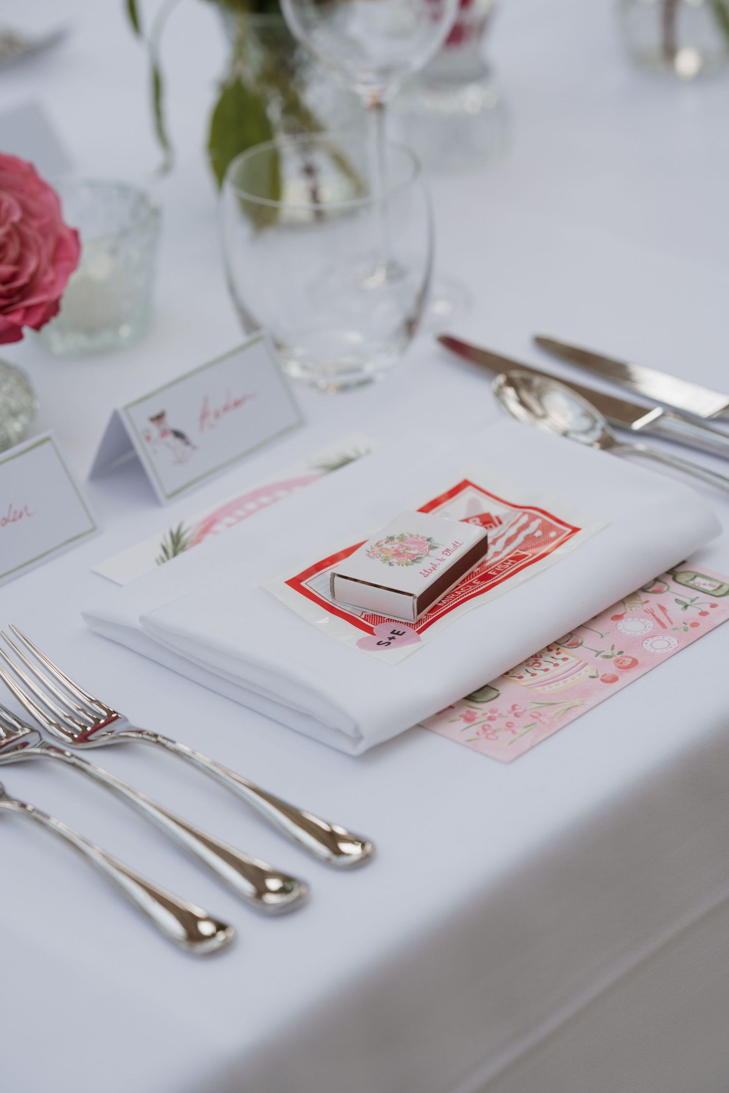 Elegant white wedding table settings with red accented place cards and silver cutlery.