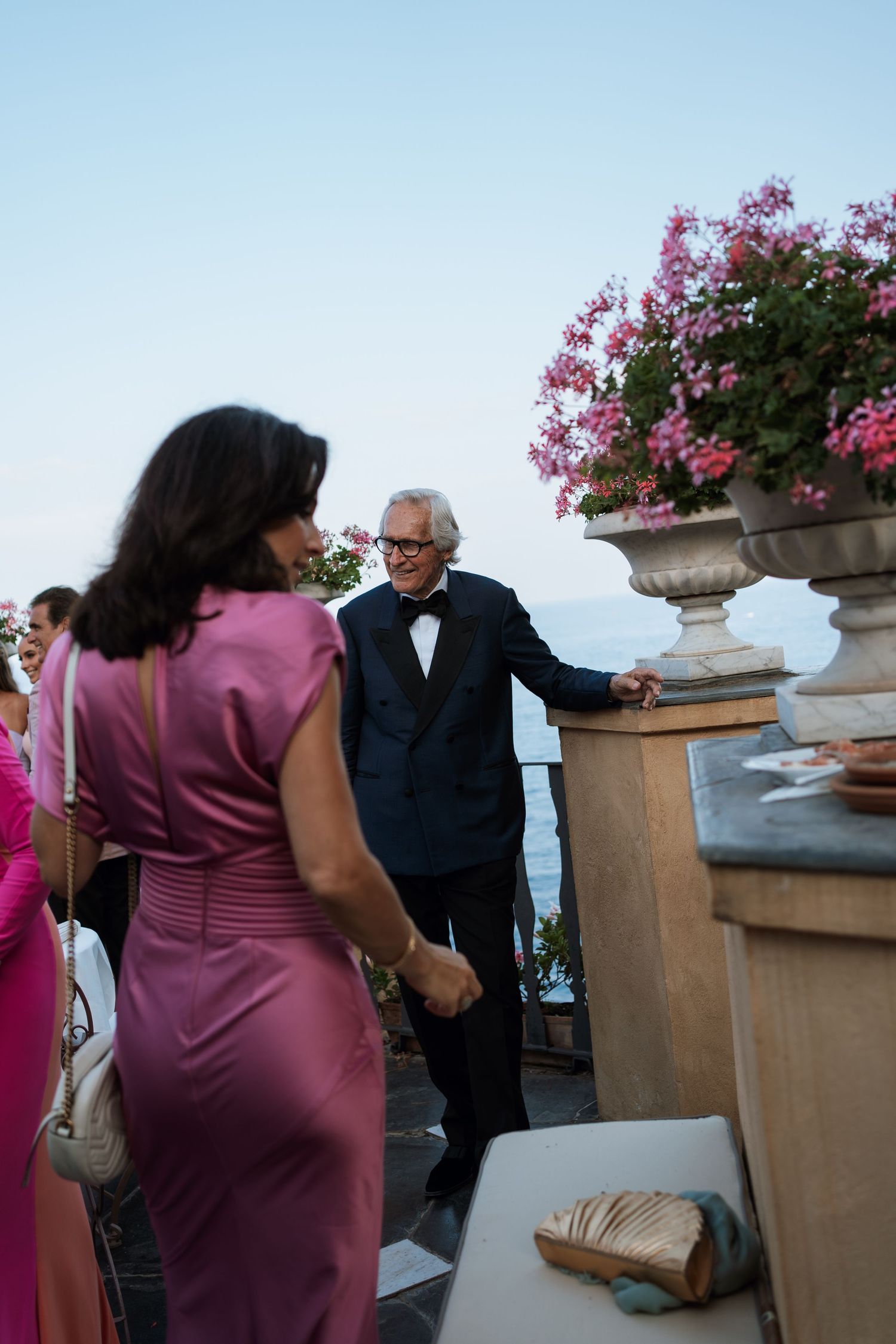 Guests mingling at an outdoor reception with pink flowers and ocean views.