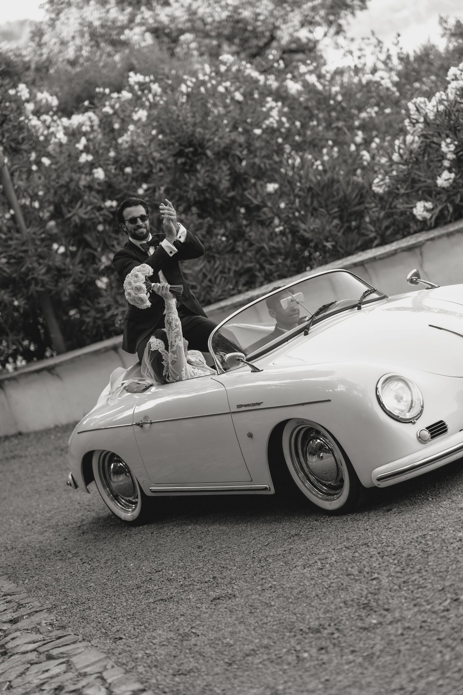 Classic vintage Porsche convertible photographed in black and white among blooming flowers.