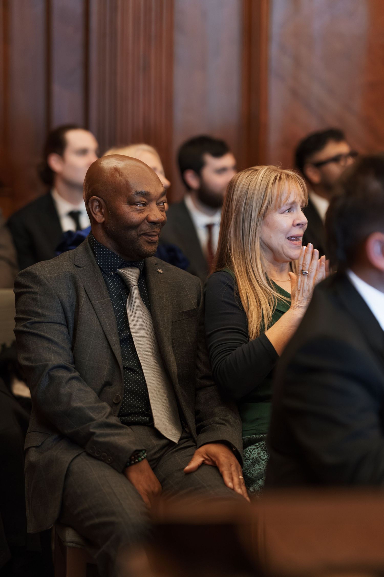 Wedding guests react emotionally during ceremony in wood-paneled venue.