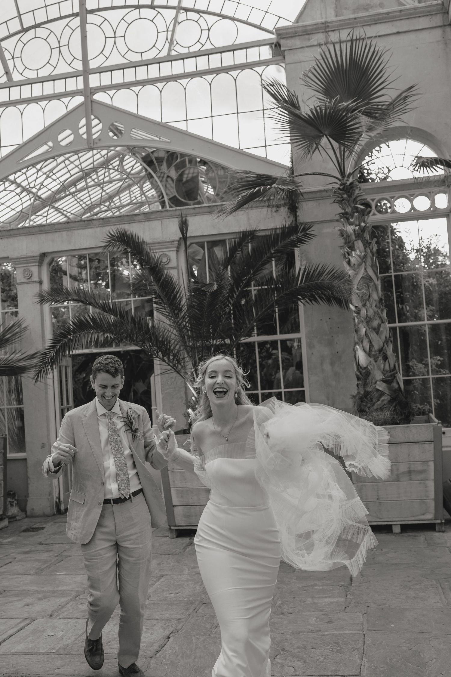 Black and white photo of a joyful couple in a Victorian-style glass conservatory.