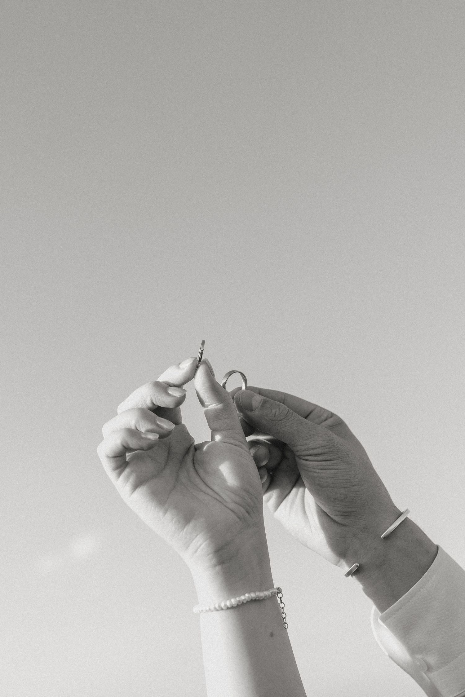 Black and white image of hands threading a needle against light background.