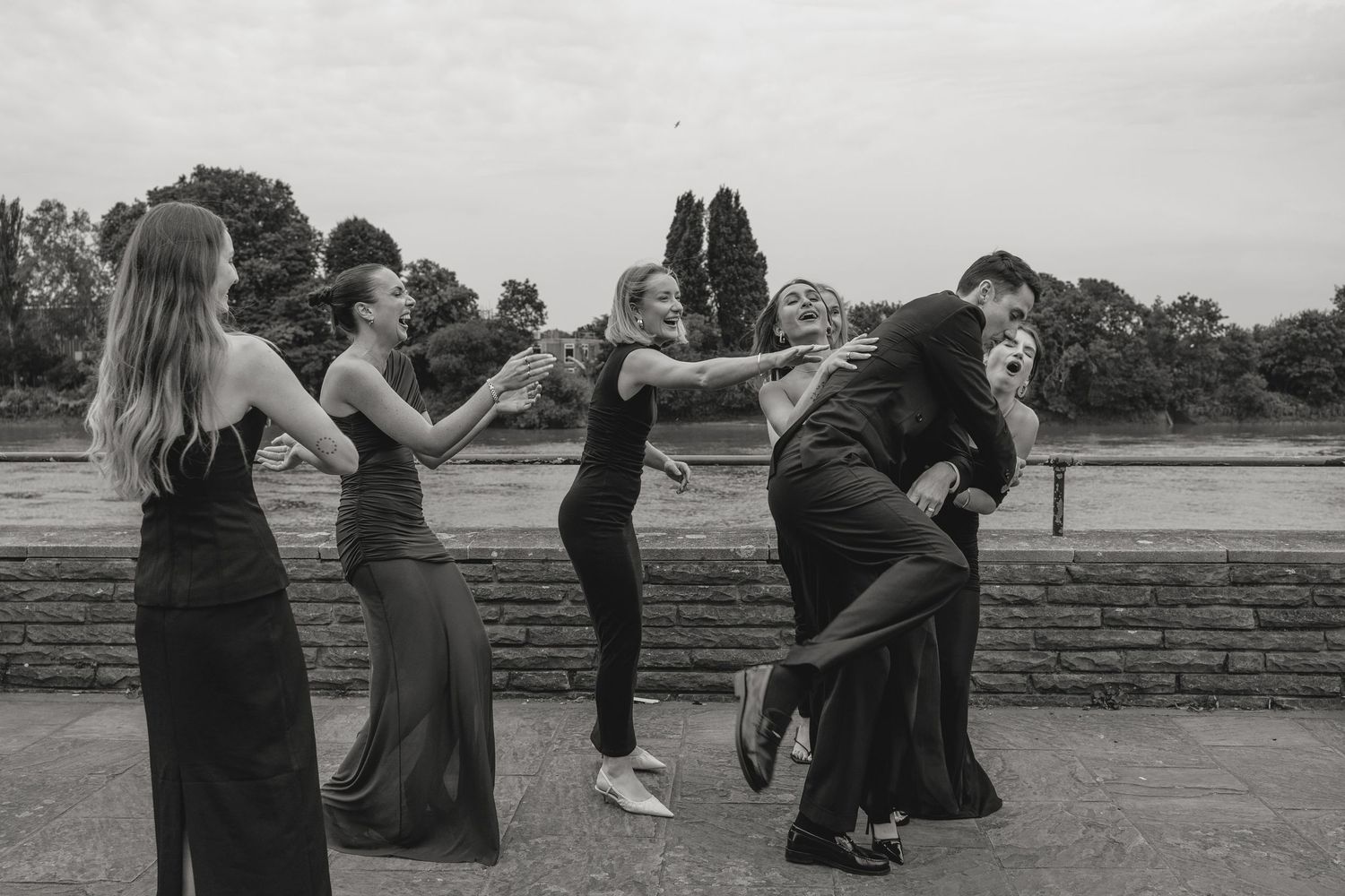 Wedding party members pose together on a stone wall outdoors.