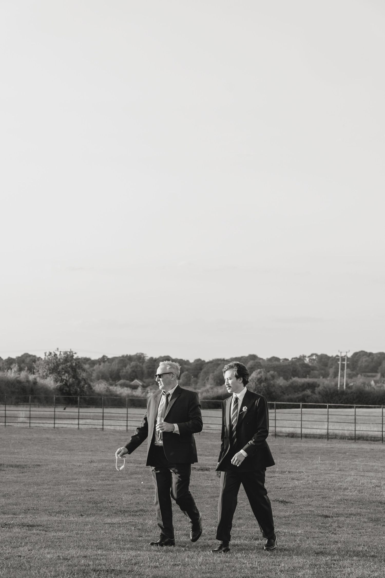 Two figures in suits playfully pose in a grassy field at sunset.