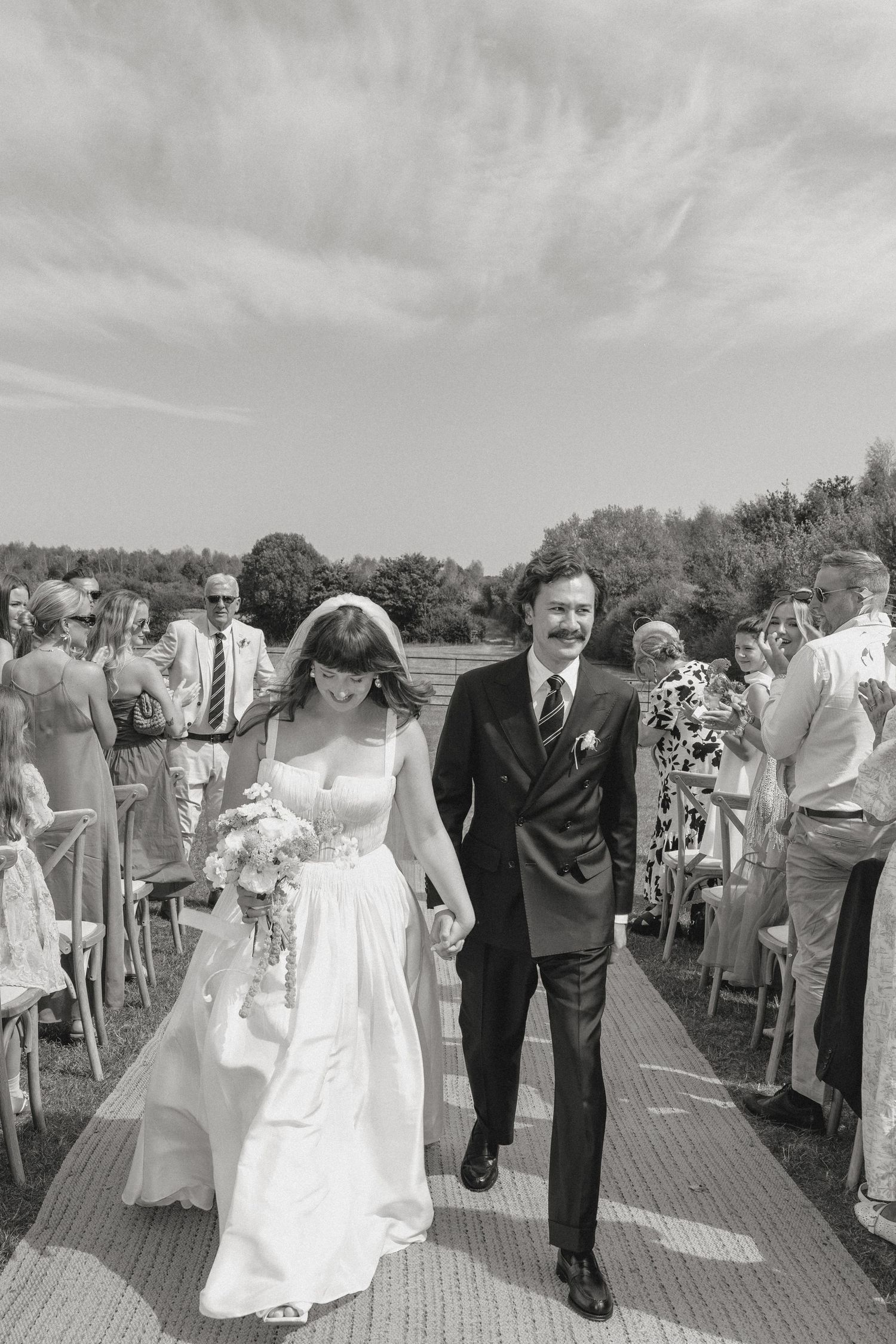 Black and white photo of wedding ceremony processional on outdoor walkway.
