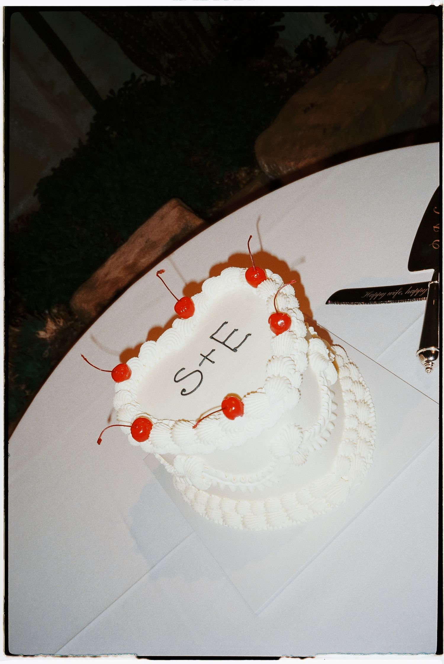 A white frosted cake decorated with red cherries on a table.