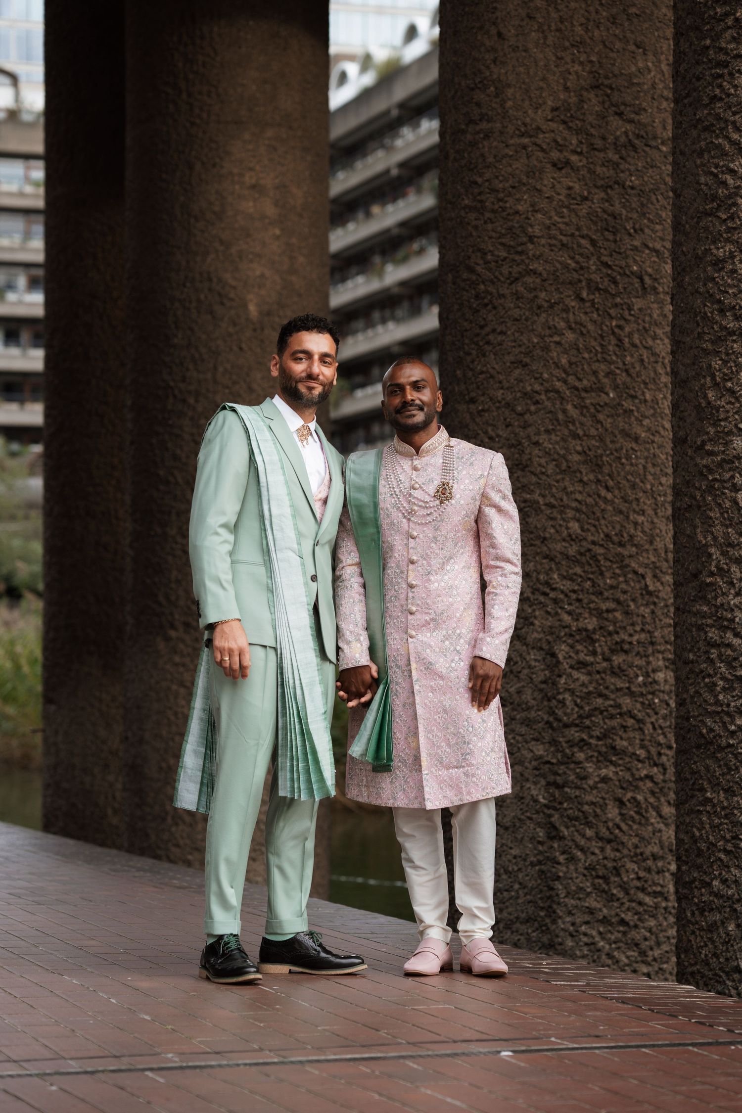 Two people in mint green and pink formal attire posing under concrete archways.