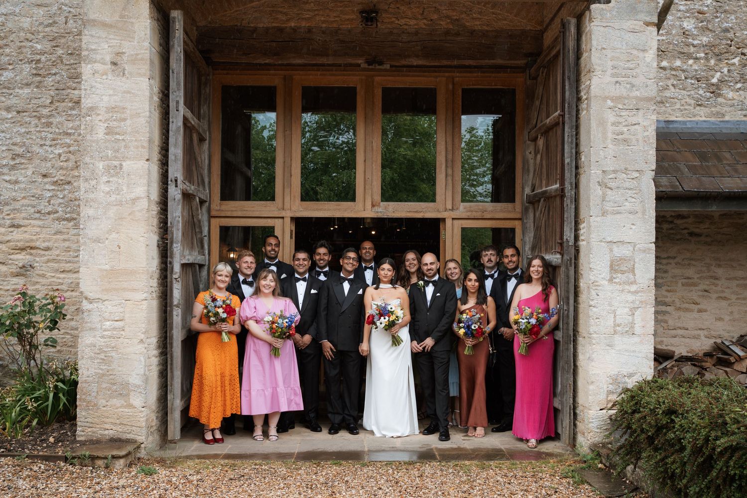 Large group wedding photo of guests gathered in front of a stone building entrance.