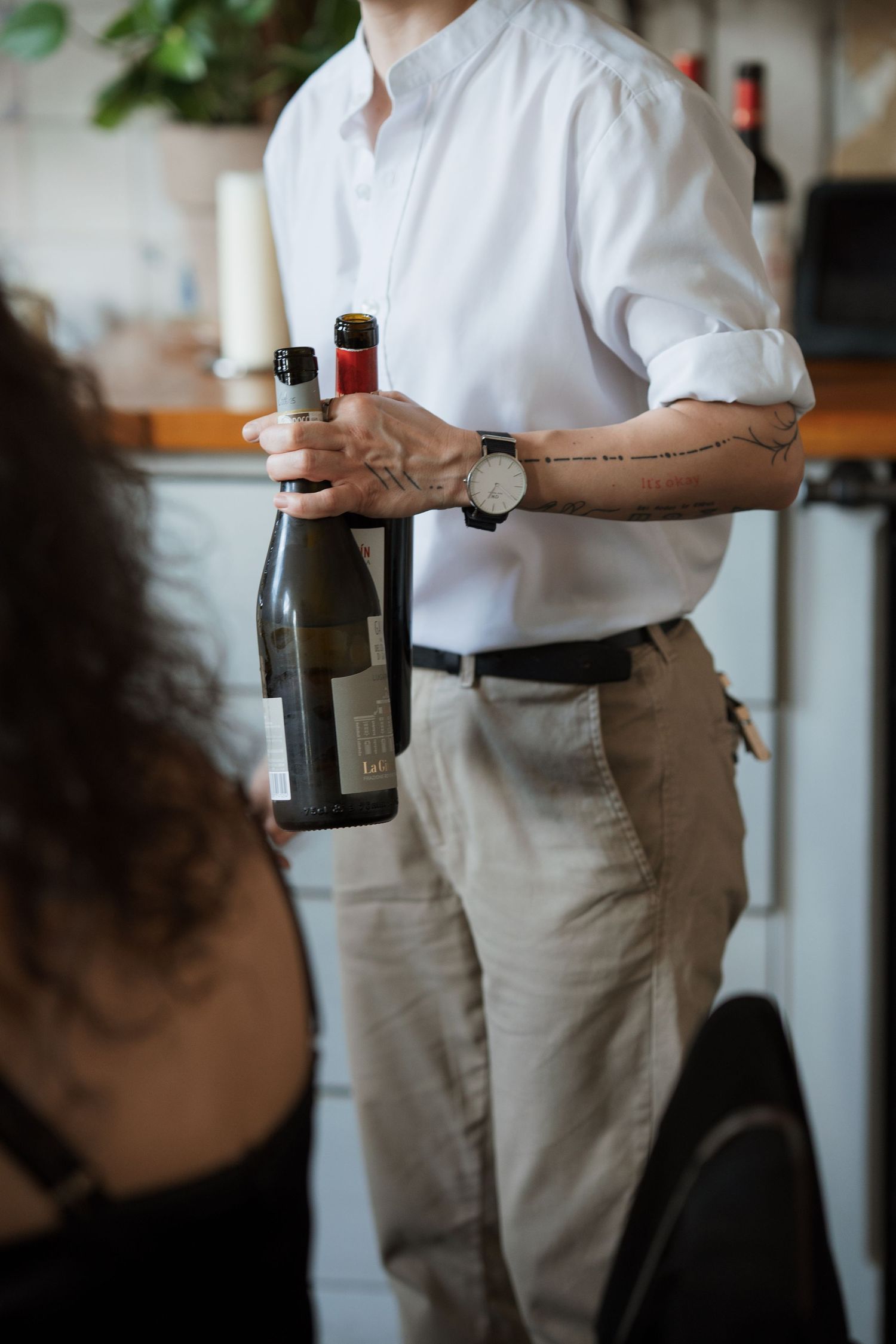 Server in white shirt and khaki pants holding wine bottles during service.