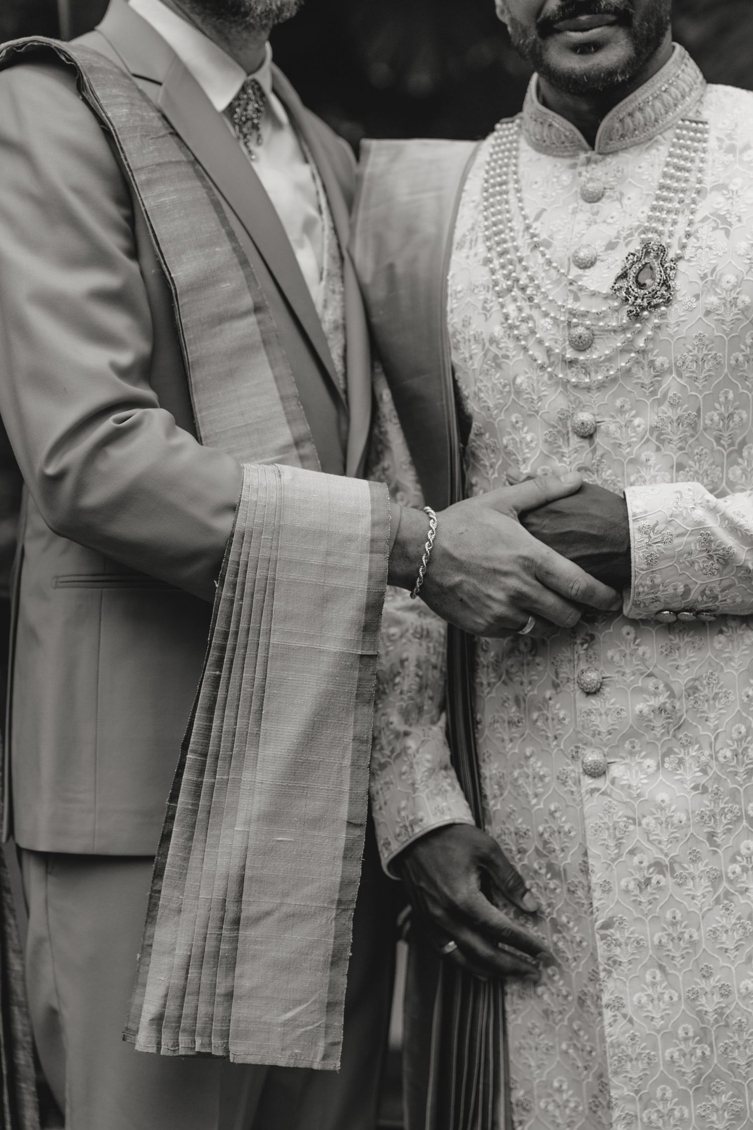 Black and white photo of two men in traditional Indian wedding attire, including sherwani with pearl necklaces.