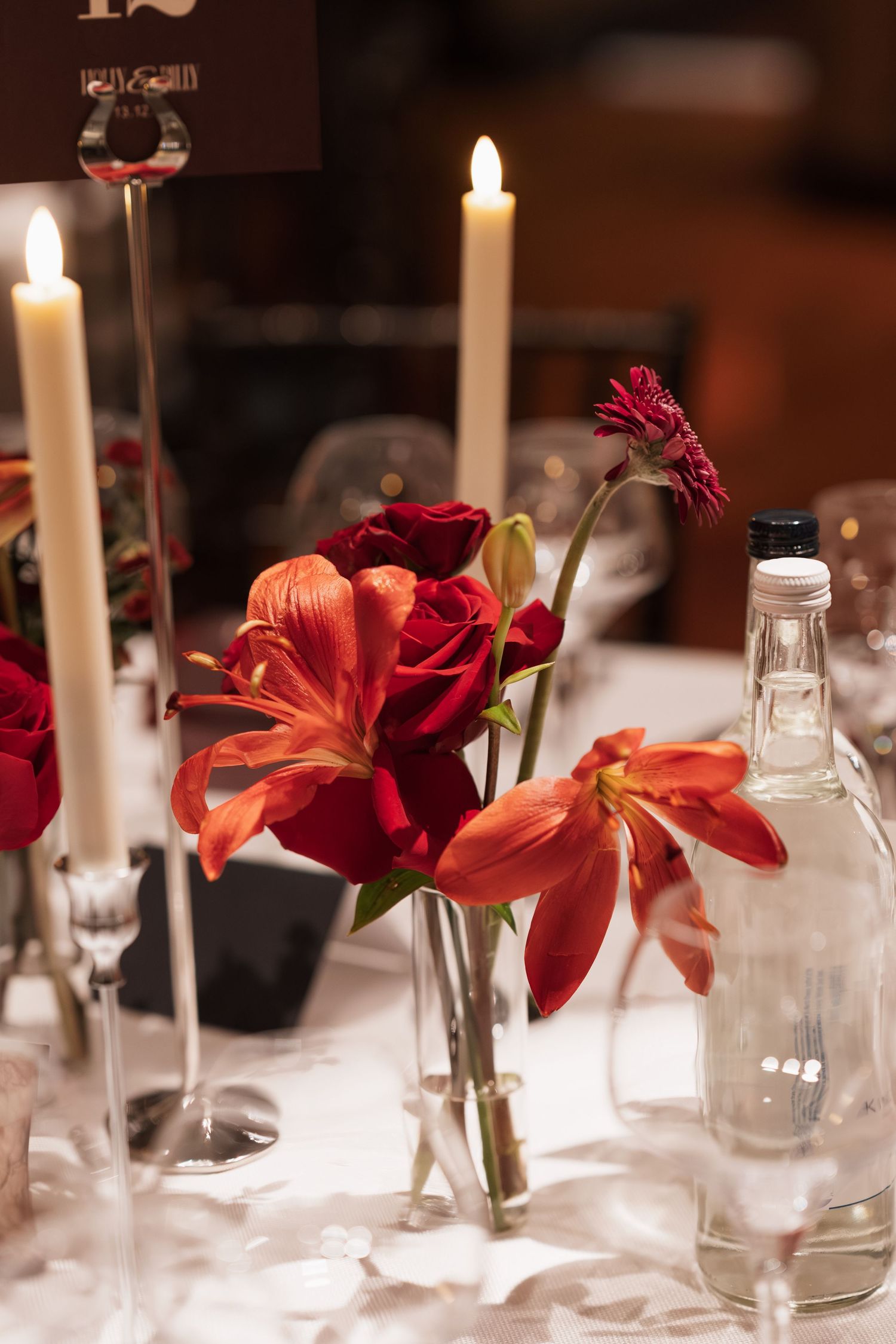 Elegant table setting with red flowers and white candles at a formal dinner.