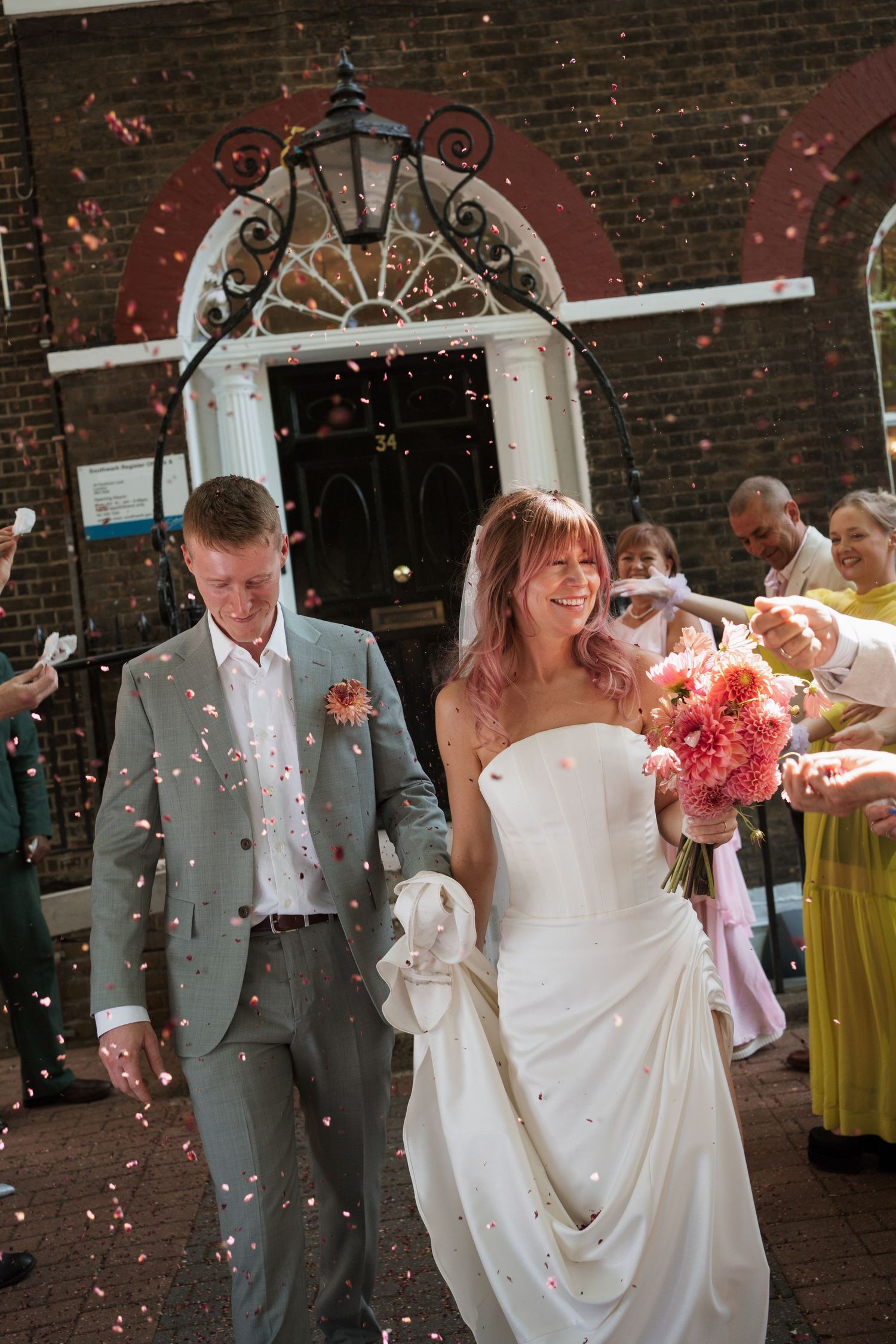 Newlyweds exiting through confetti shower under ornate brick archway.