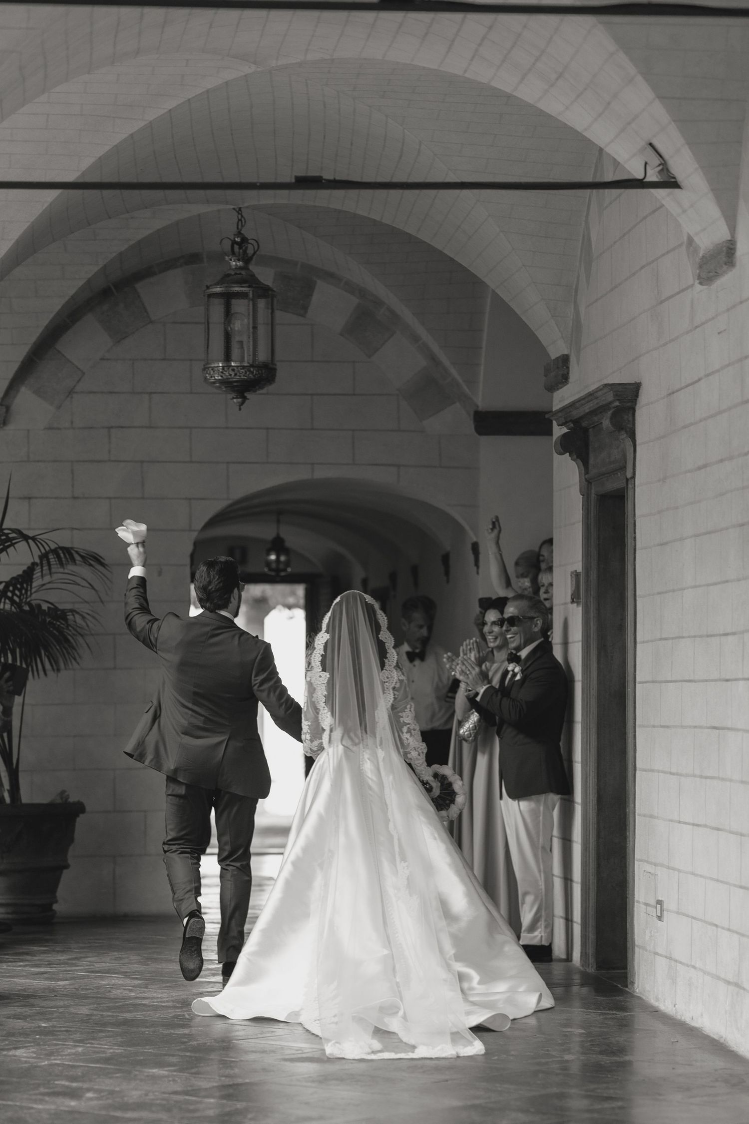 Elegant wedding couple photographed in sequence under arched hallway in black and white.
