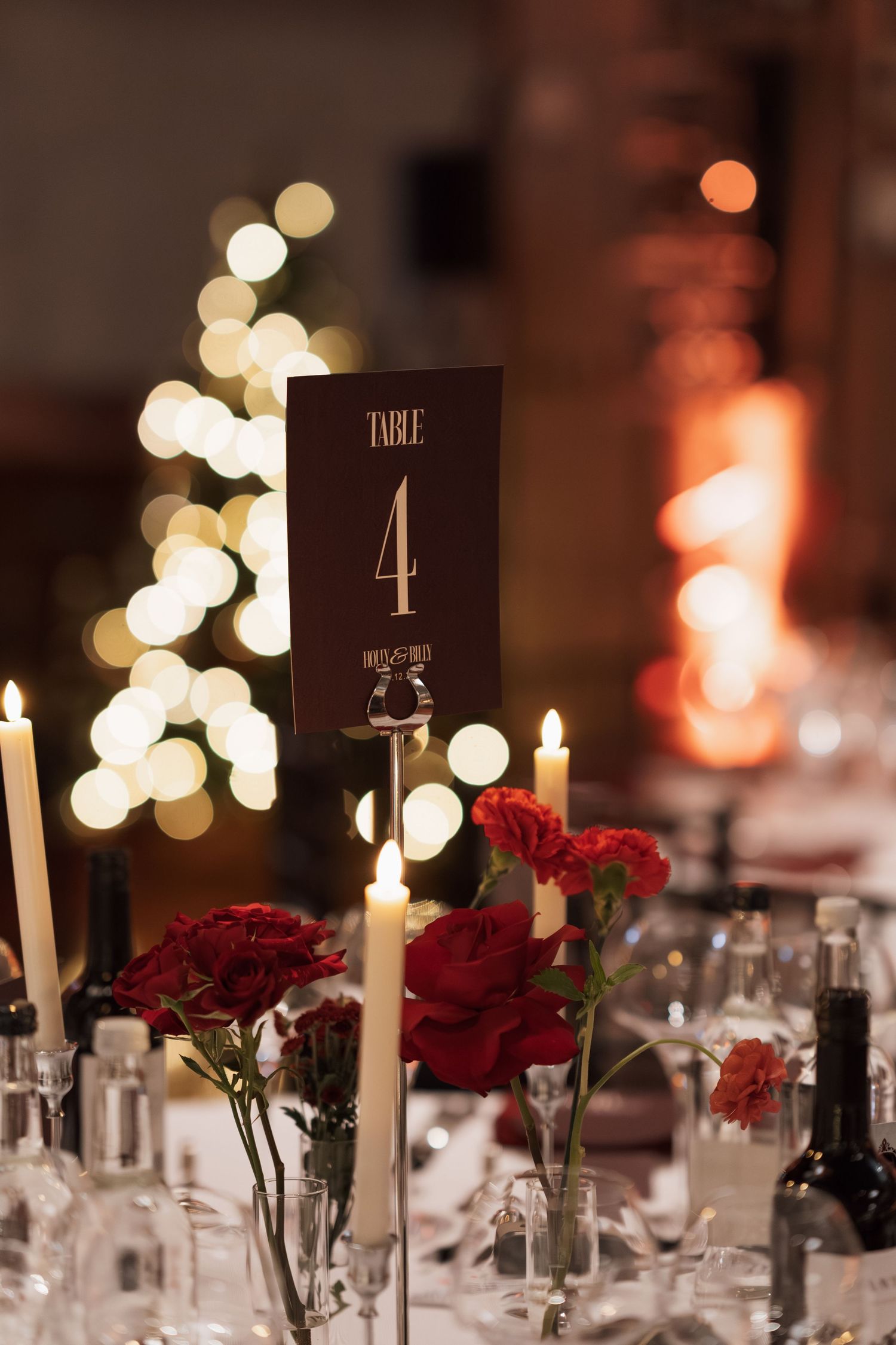 Elegant table setting with red roses, candles and numbered table markers at a formal dinner.