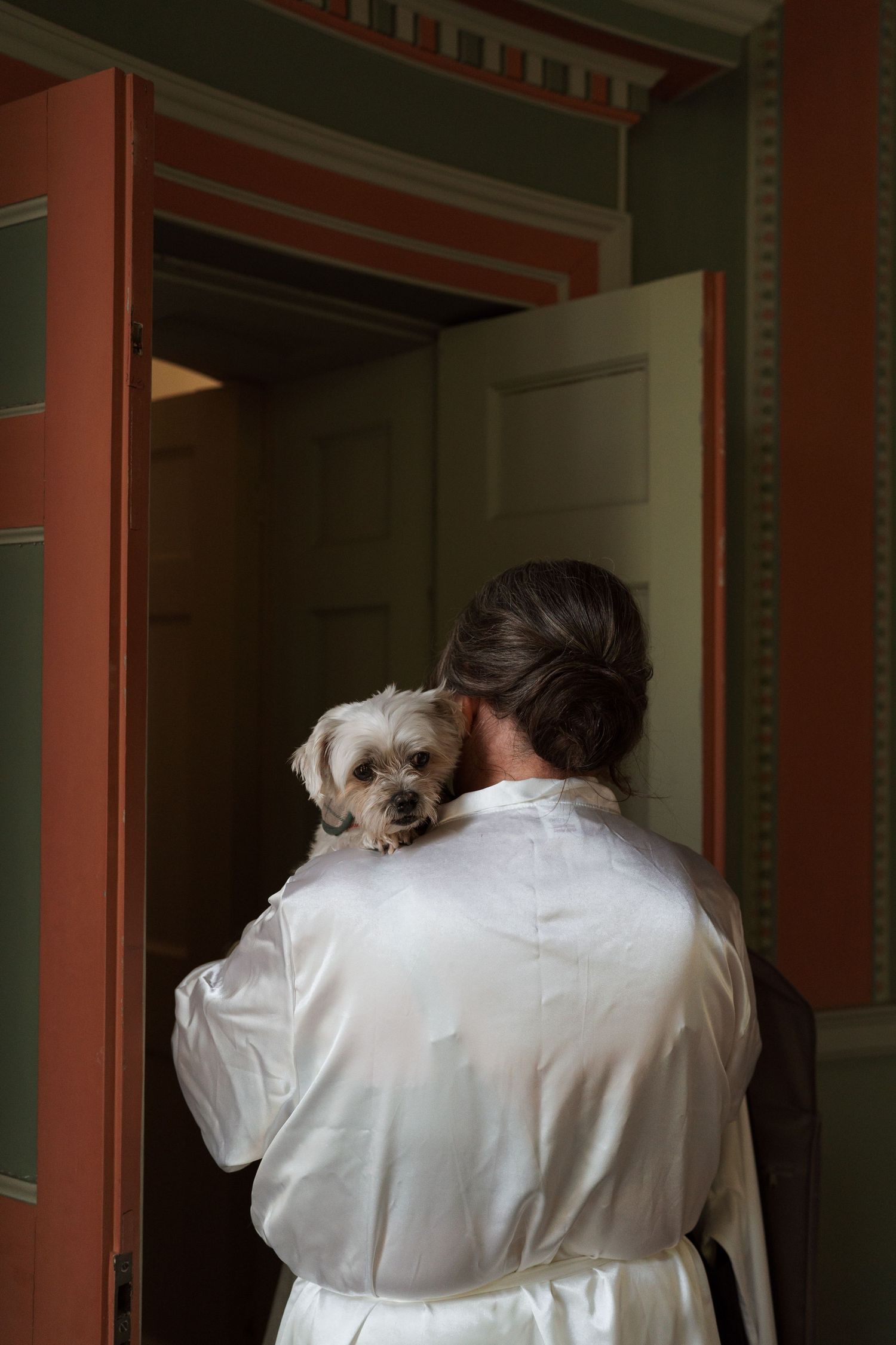Person in white robe hugging small dog in dimly lit interior setting.