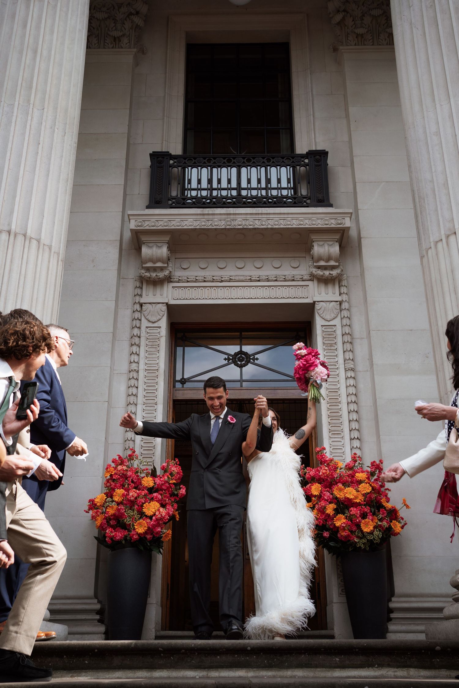 Wedding party poses on grand stone steps with vibrant floral arrangements.