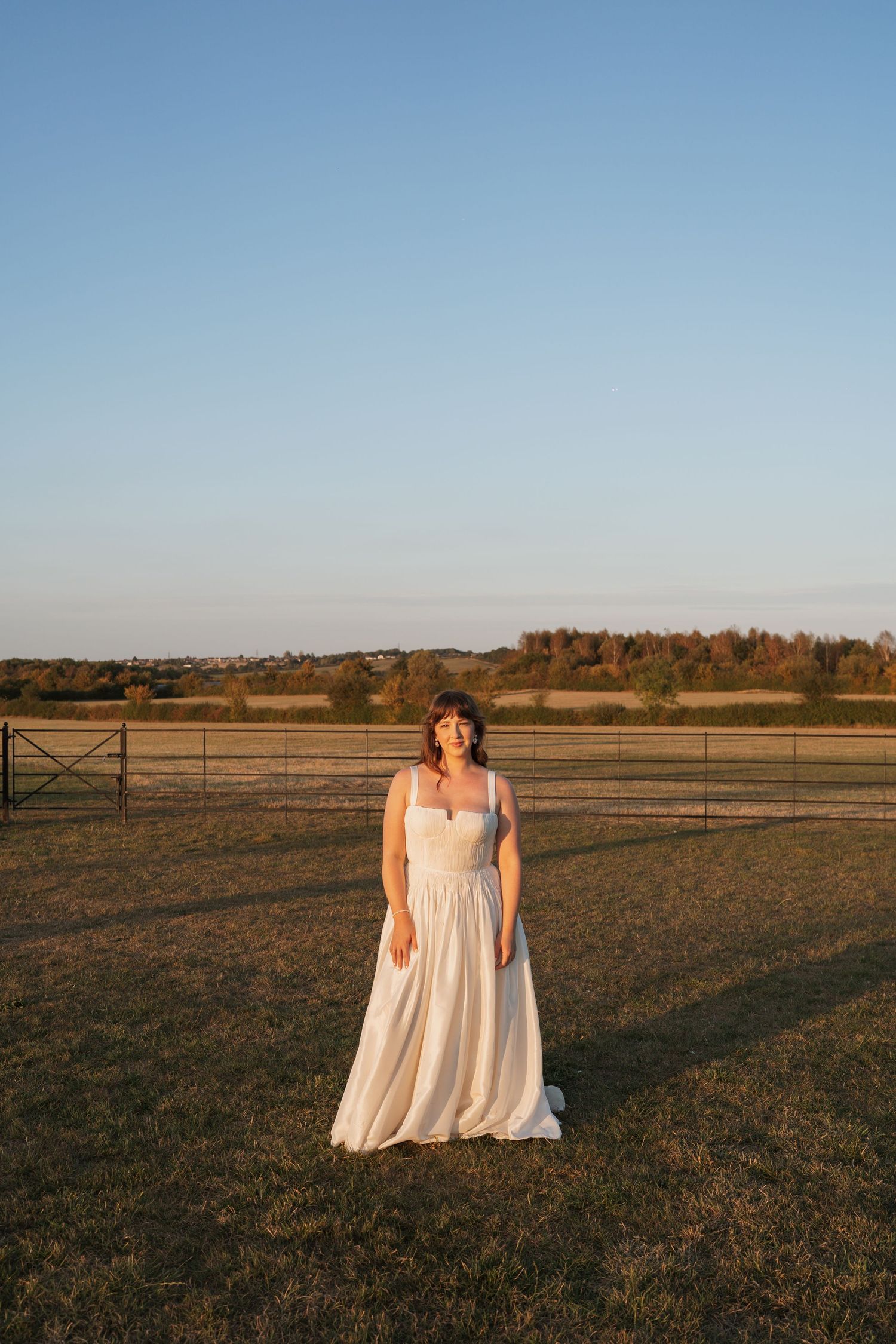 Couple in wedding attire standing in a vast open field during golden hour.