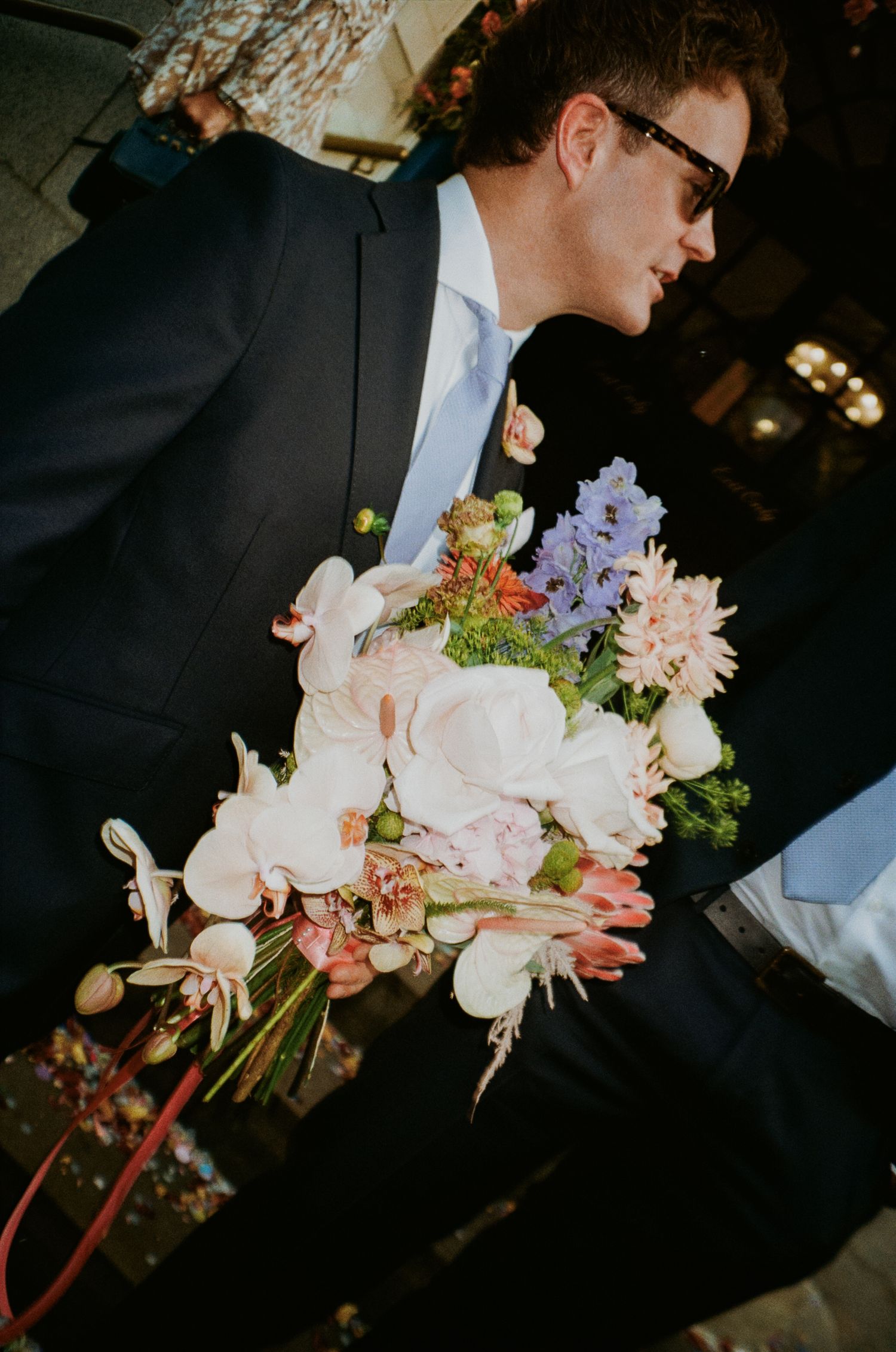 Person in formal attire holding an elegant bouquet of mixed flowers.