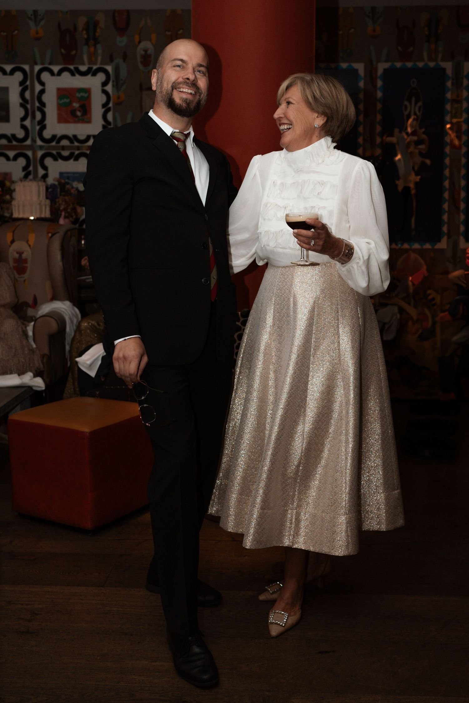 Two people dancing together at a party with decorative wall patterns in the background.