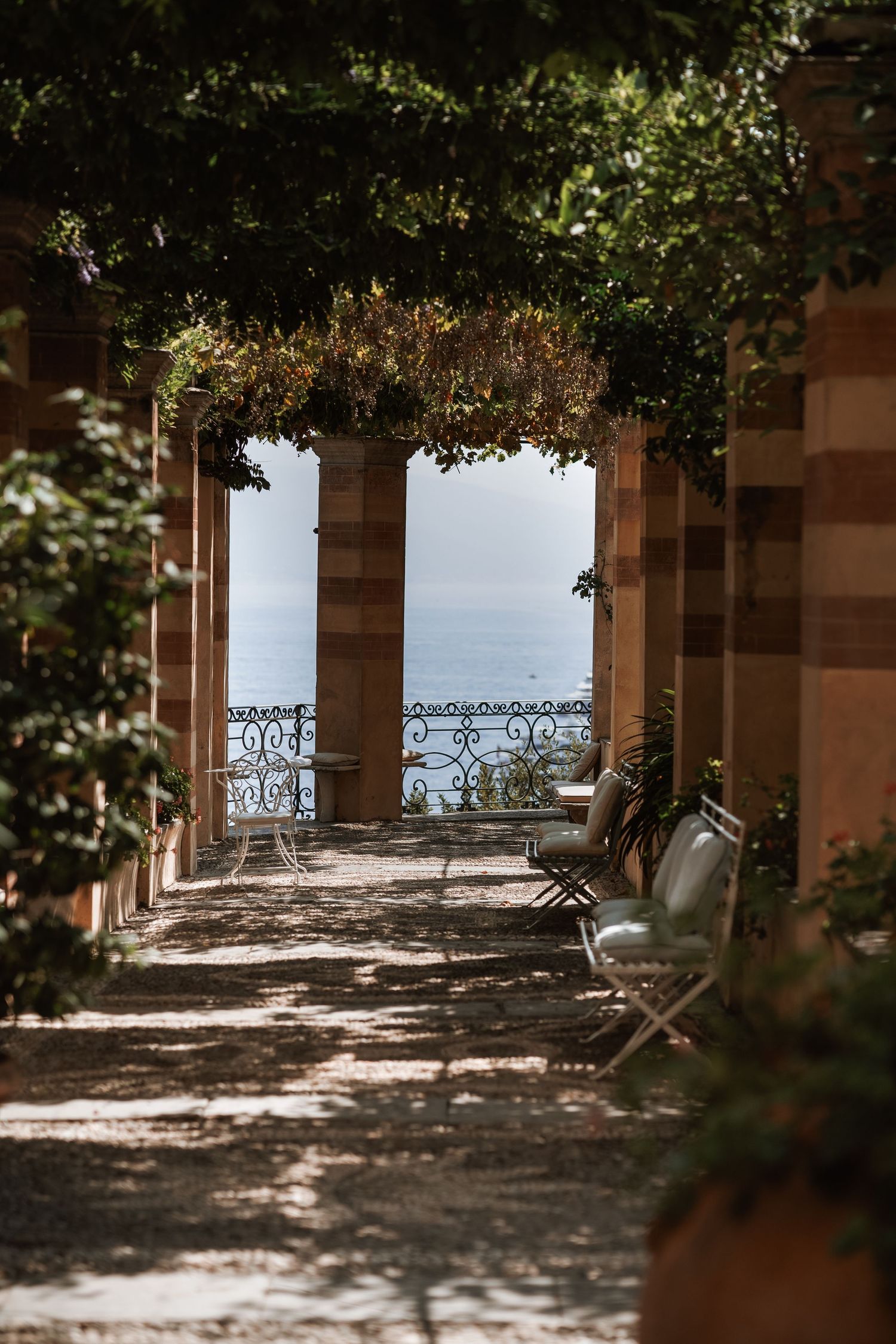 Covered terrace with ornate iron railings overlooking a scenic waterfront view.