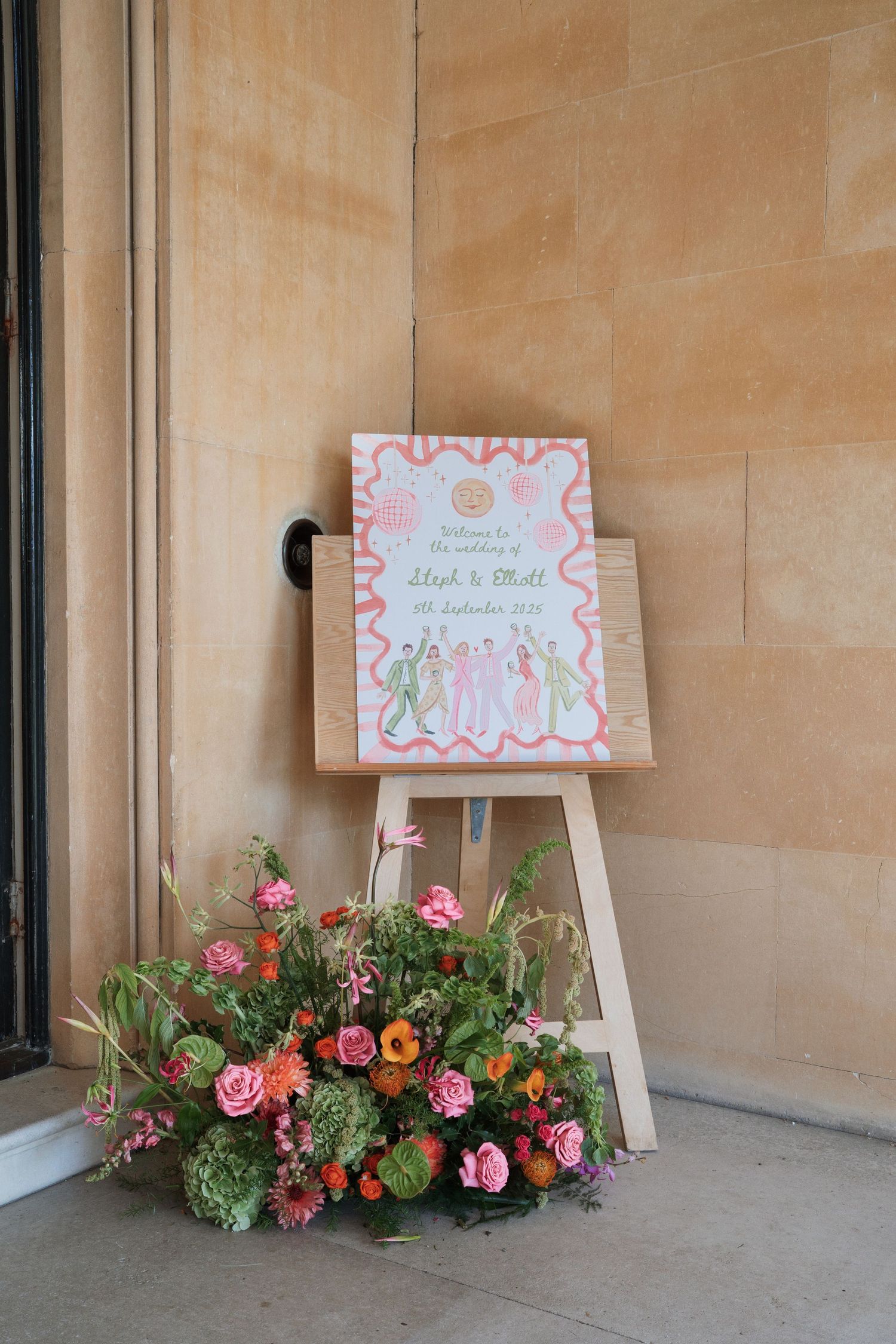 Wedding signage and floral arrangements displayed against stone wall.